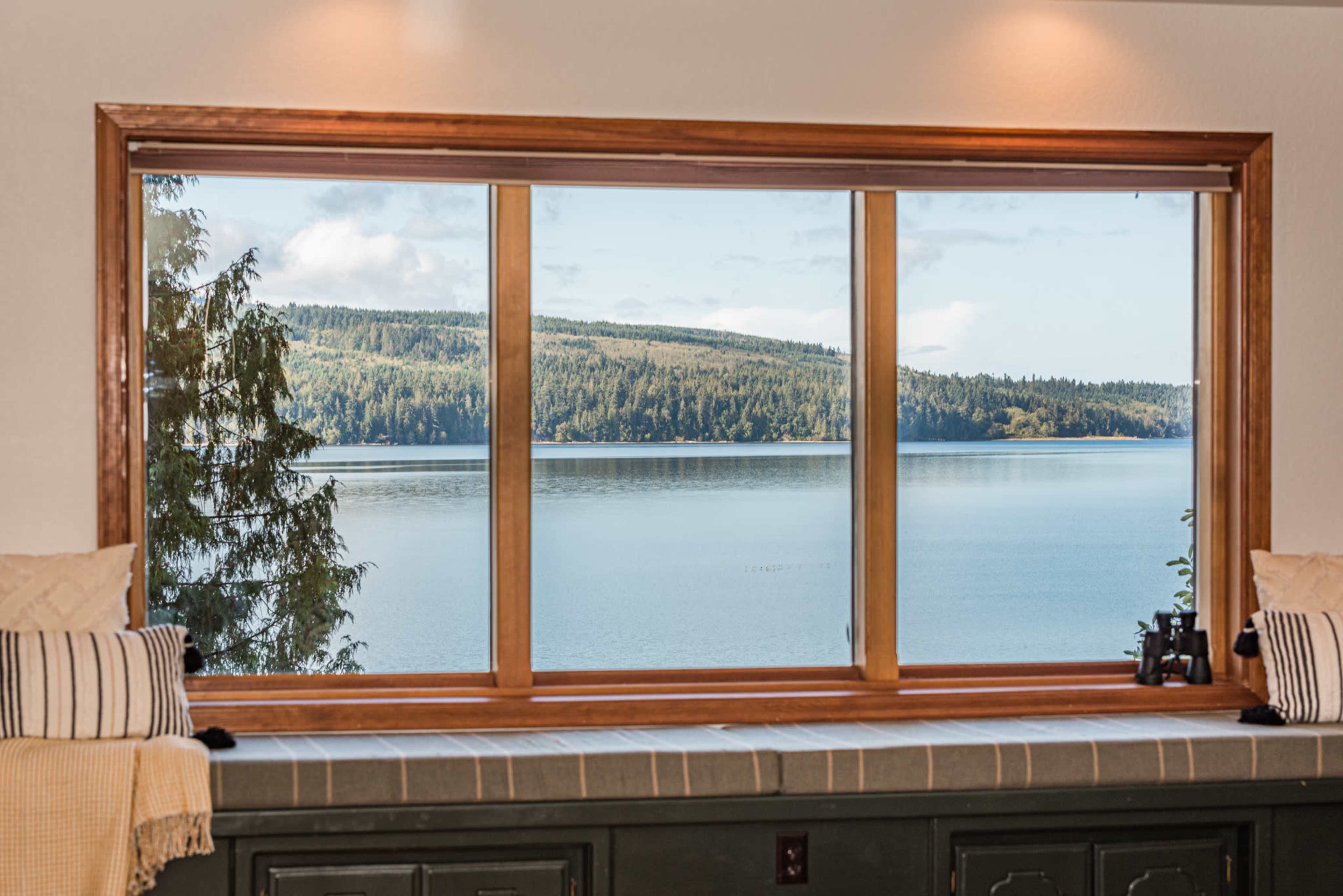 A large wooden window framing a view of a calm lake and forested hills in the background.