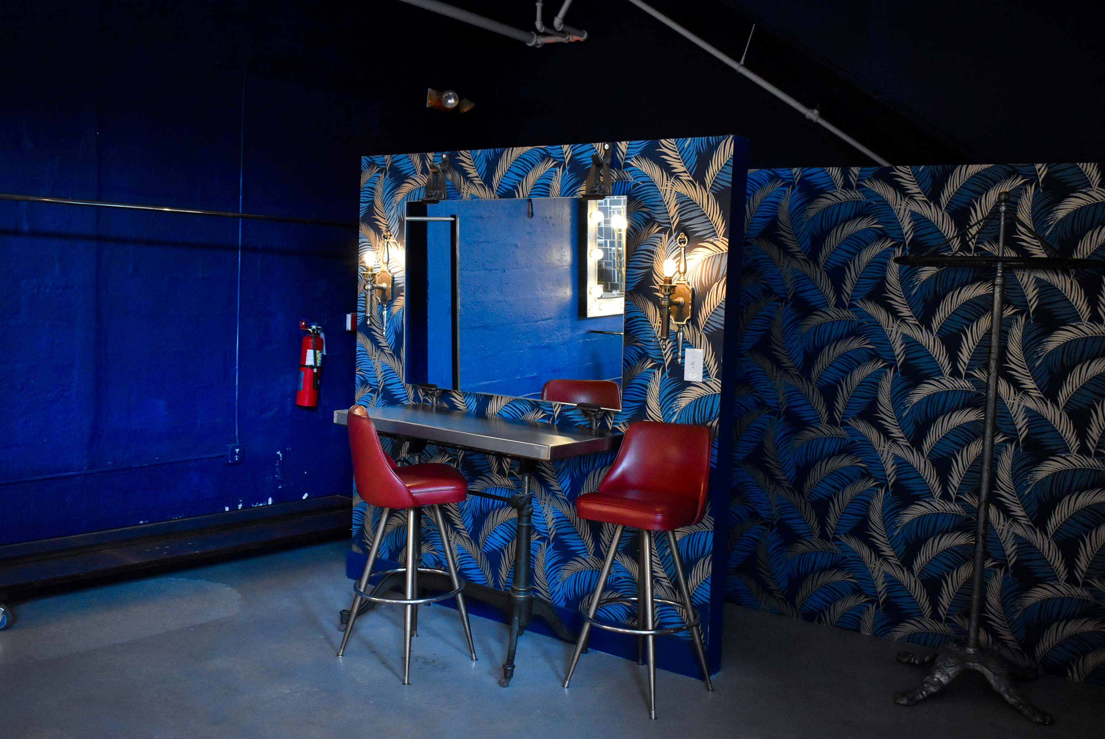 A bar area with a mirrored wall and two red stools, surrounded by blue and cream patterned wallpaper.