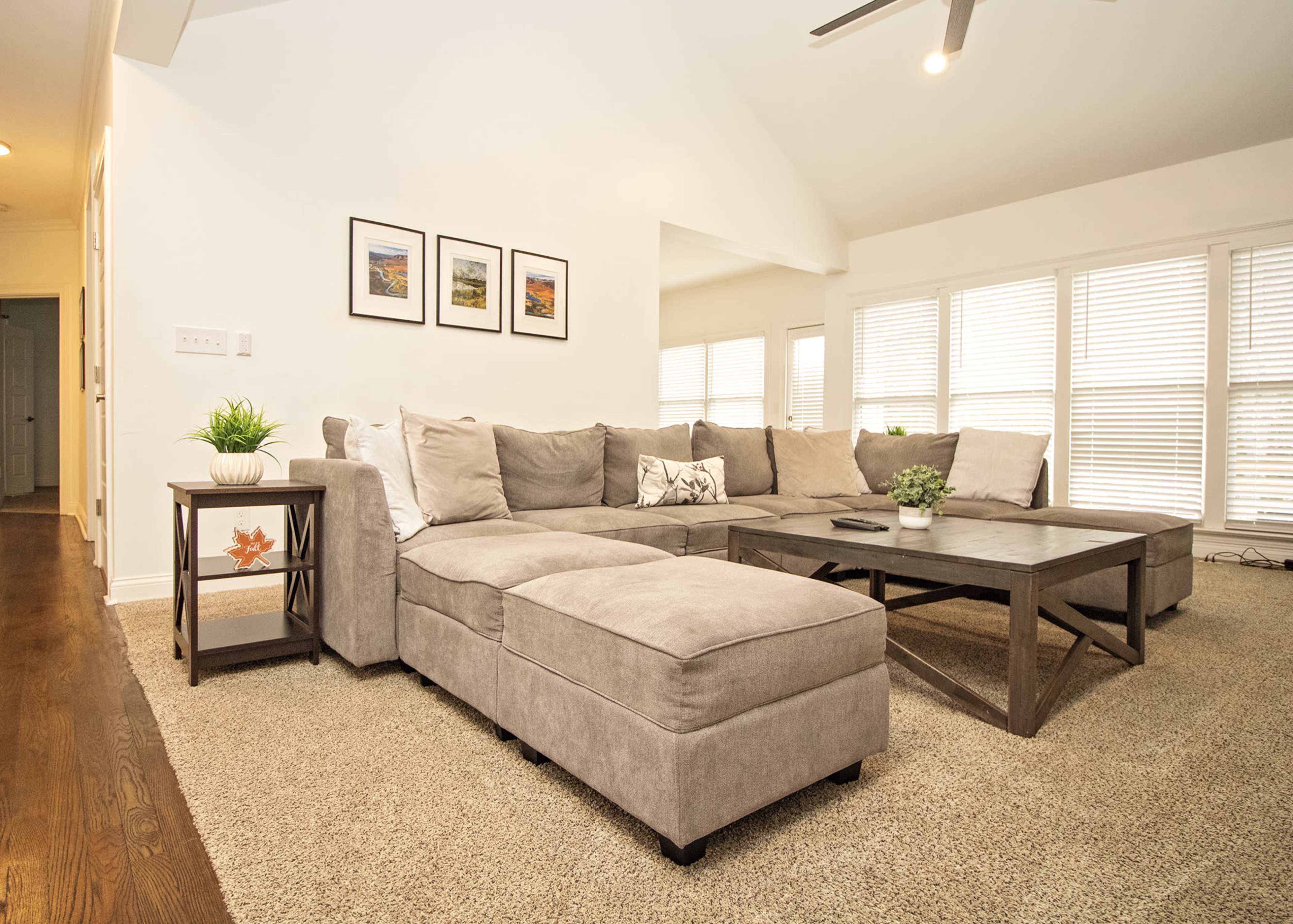 A large, light-colored sectional sofa sits in a well-lit living room with a coffee table and framed pictures on the wall.