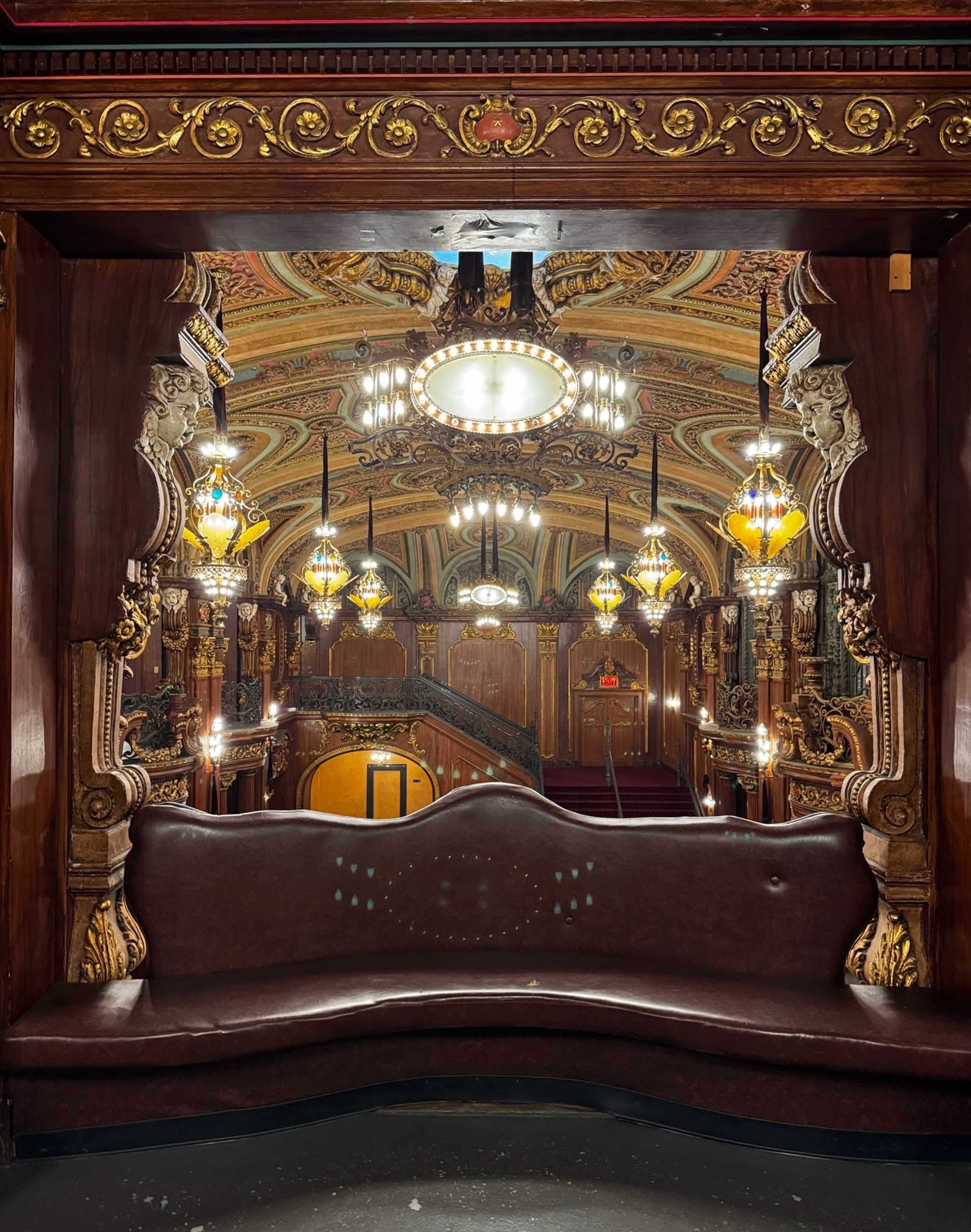 The image shows a vintage theater interior featuring ornate decorations, decorative lighting fixtures, and an elegant staircase in the background.