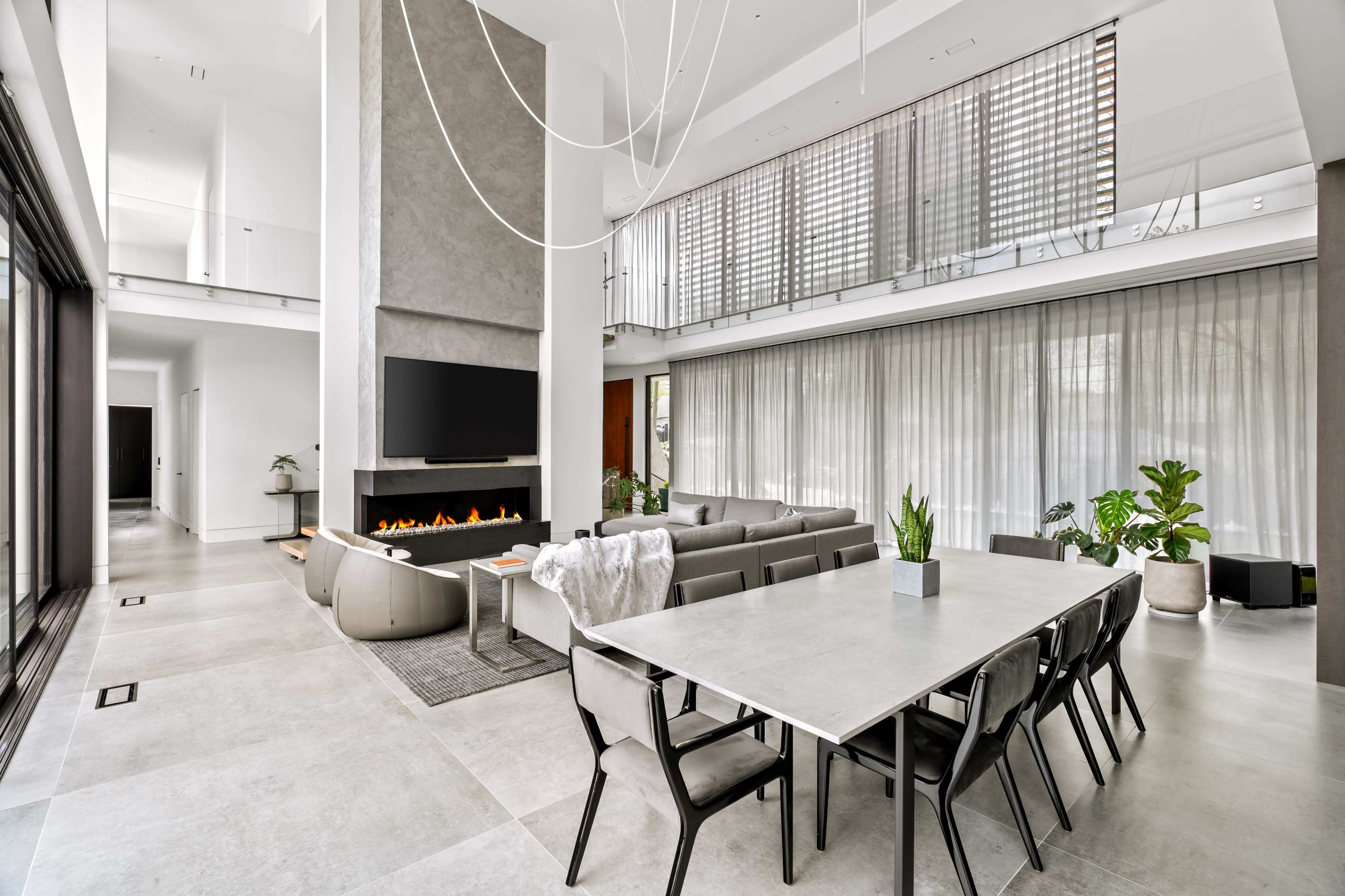 The image showcases a modern living space featuring a spacious open layout with a dining table, a sofa area, a fireplace, and large windows allowing natural light to enter.