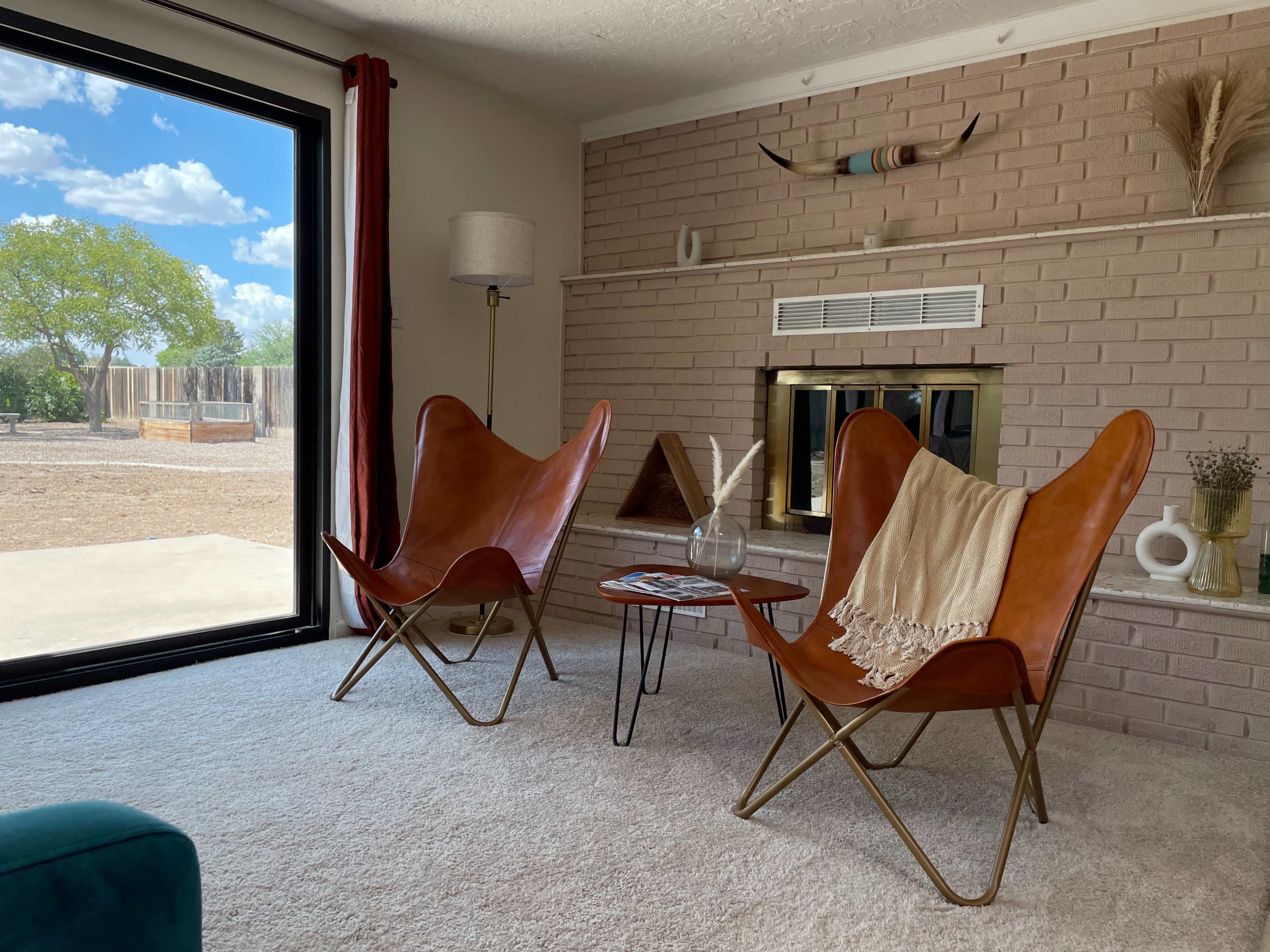 A living room with two brown leather butterfly chairs facing a small side table, a fireplace, and large sliding glass doors opening to an outdoor area.