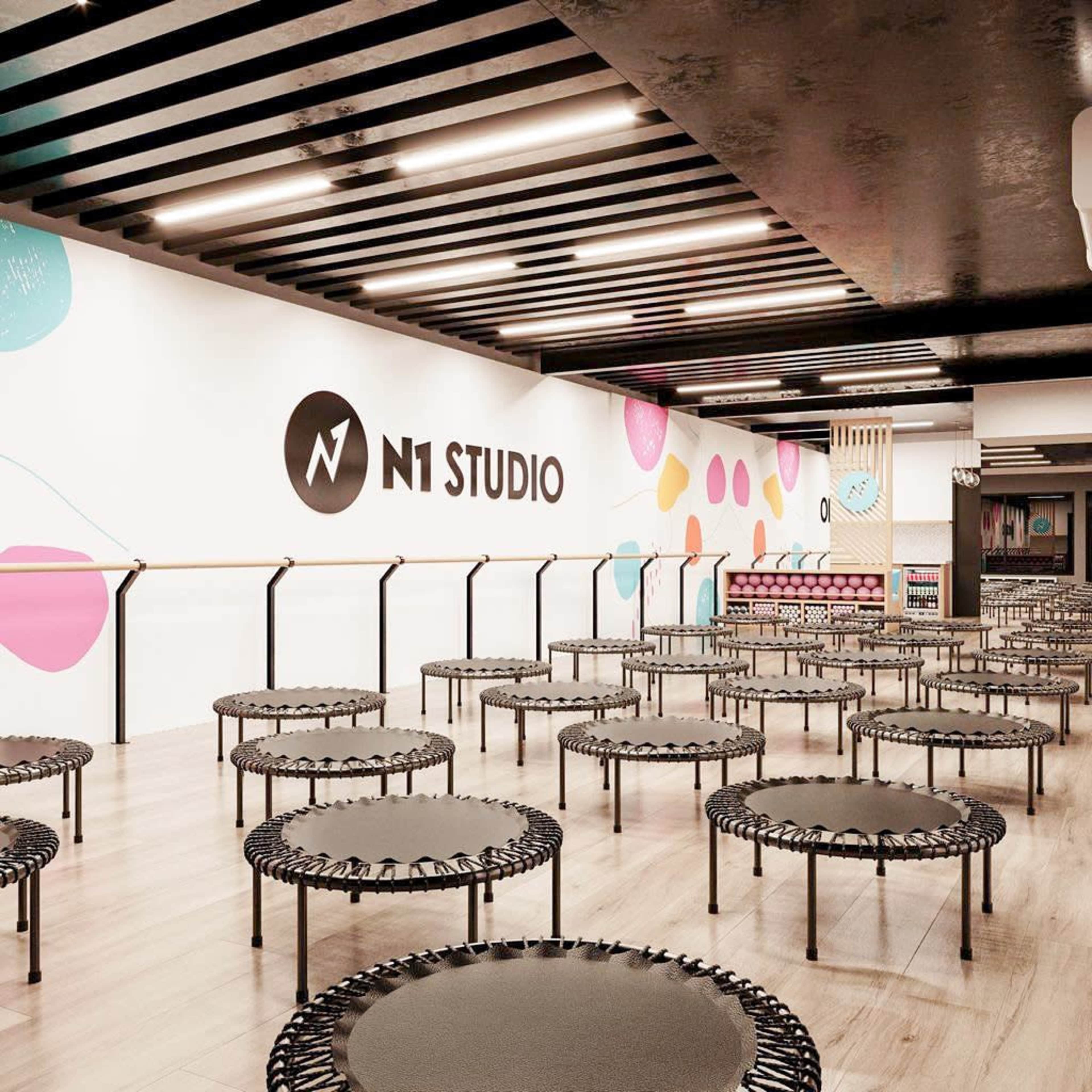 The image shows an exercise studio with numerous small trampolines arranged in rows, featuring a colorful mural on the wall and a modern design.