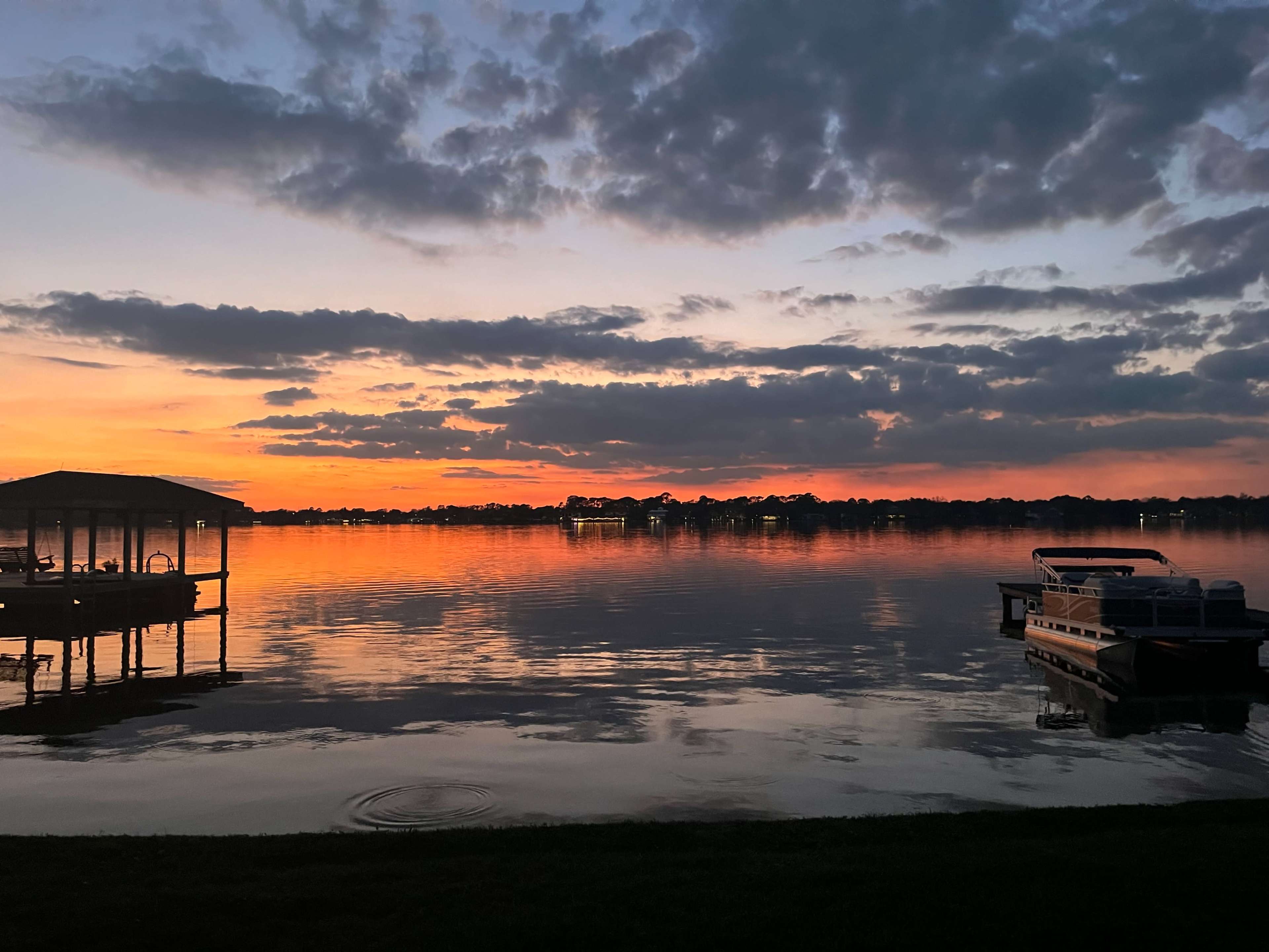 The image shows a tranquil lake at sunset, with a dock on the left and a boat moored on the right, reflecting colorful clouds in the water.