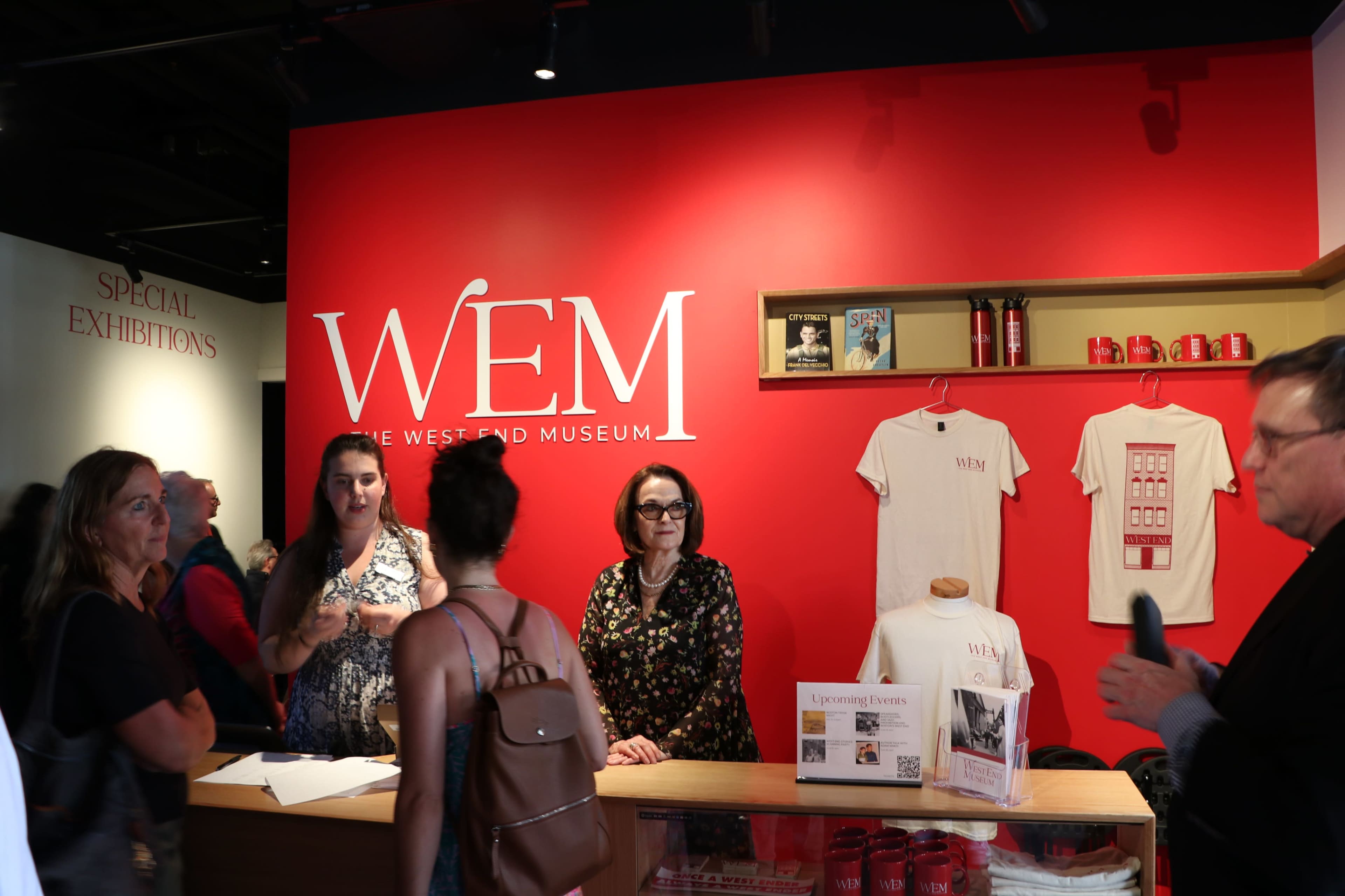 A reception area of the West End Museum, featuring a red wall with the museum's logo and merchandise for sale.