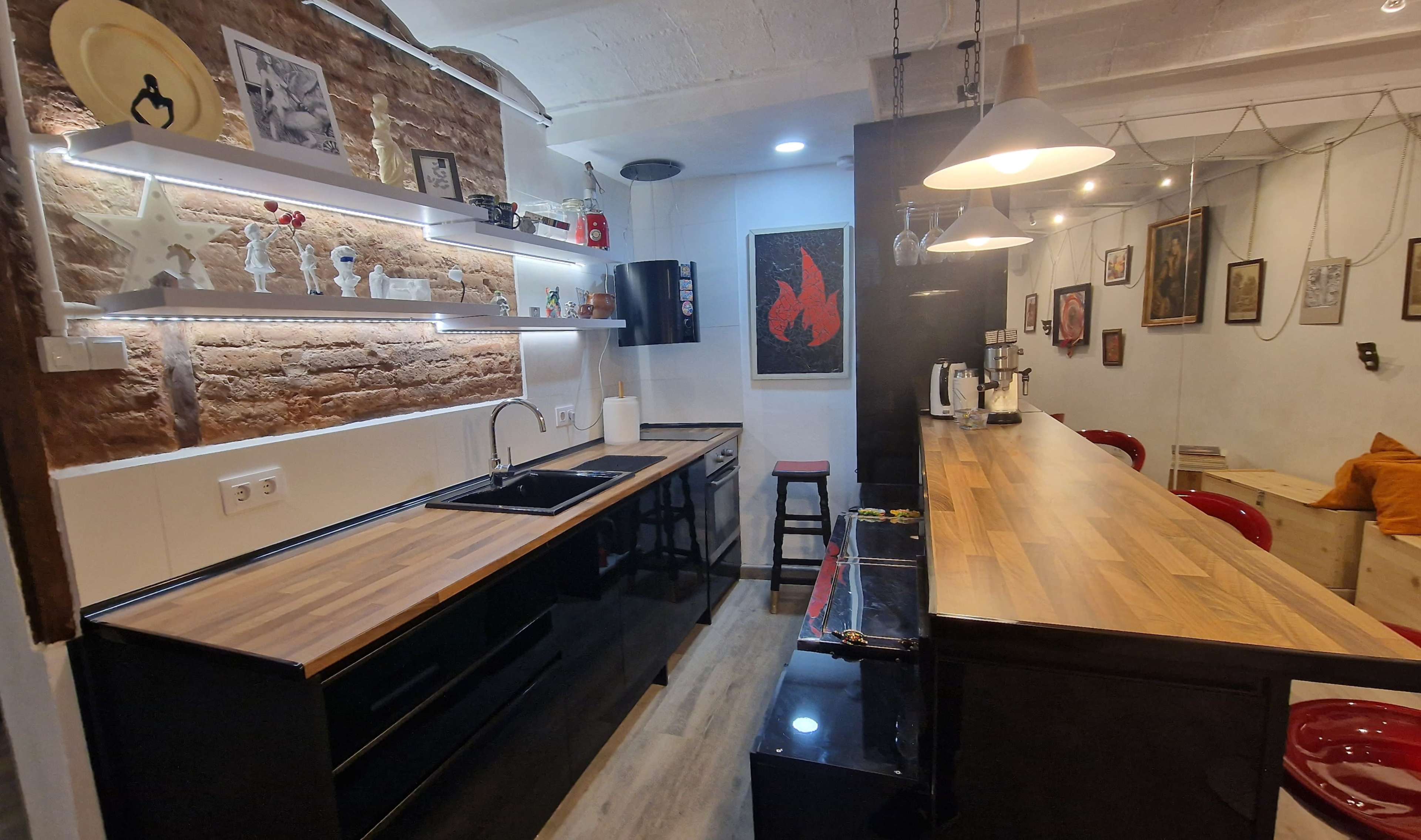 A modern kitchen with a wooden countertop, black cabinets, and exposed brick walls.