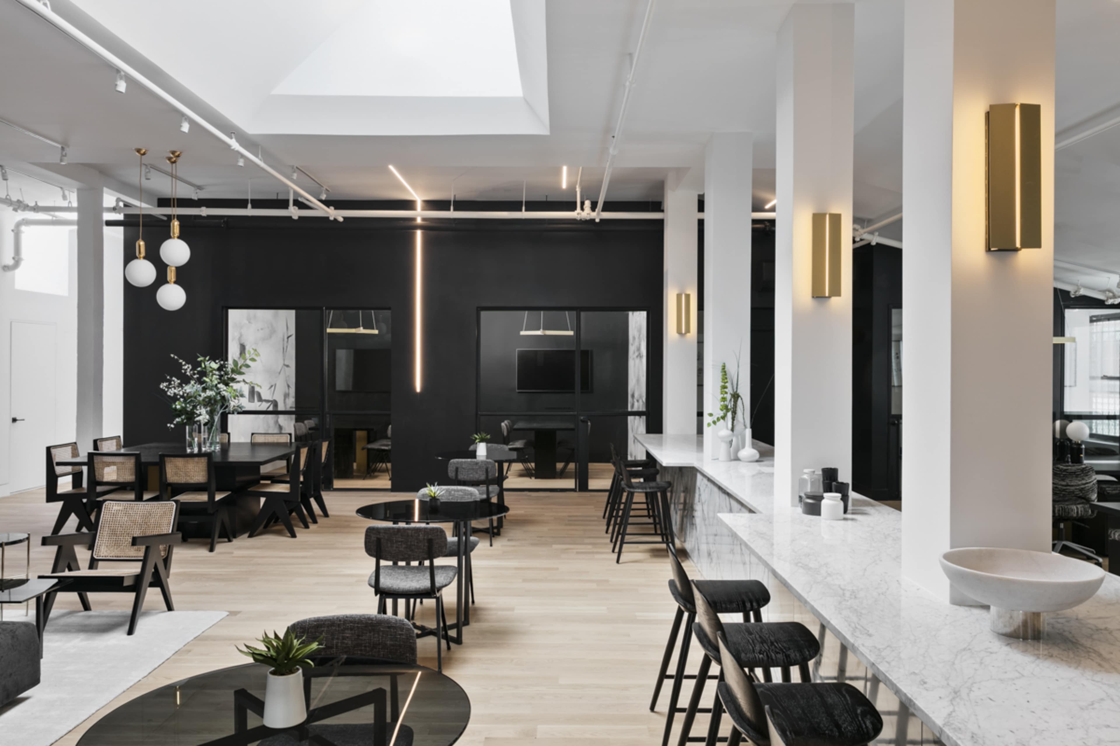 A modern interior space featuring a combination of dining tables and chairs, a sleek bar area with a marble countertop, and large windows allowing natural light to enter.
