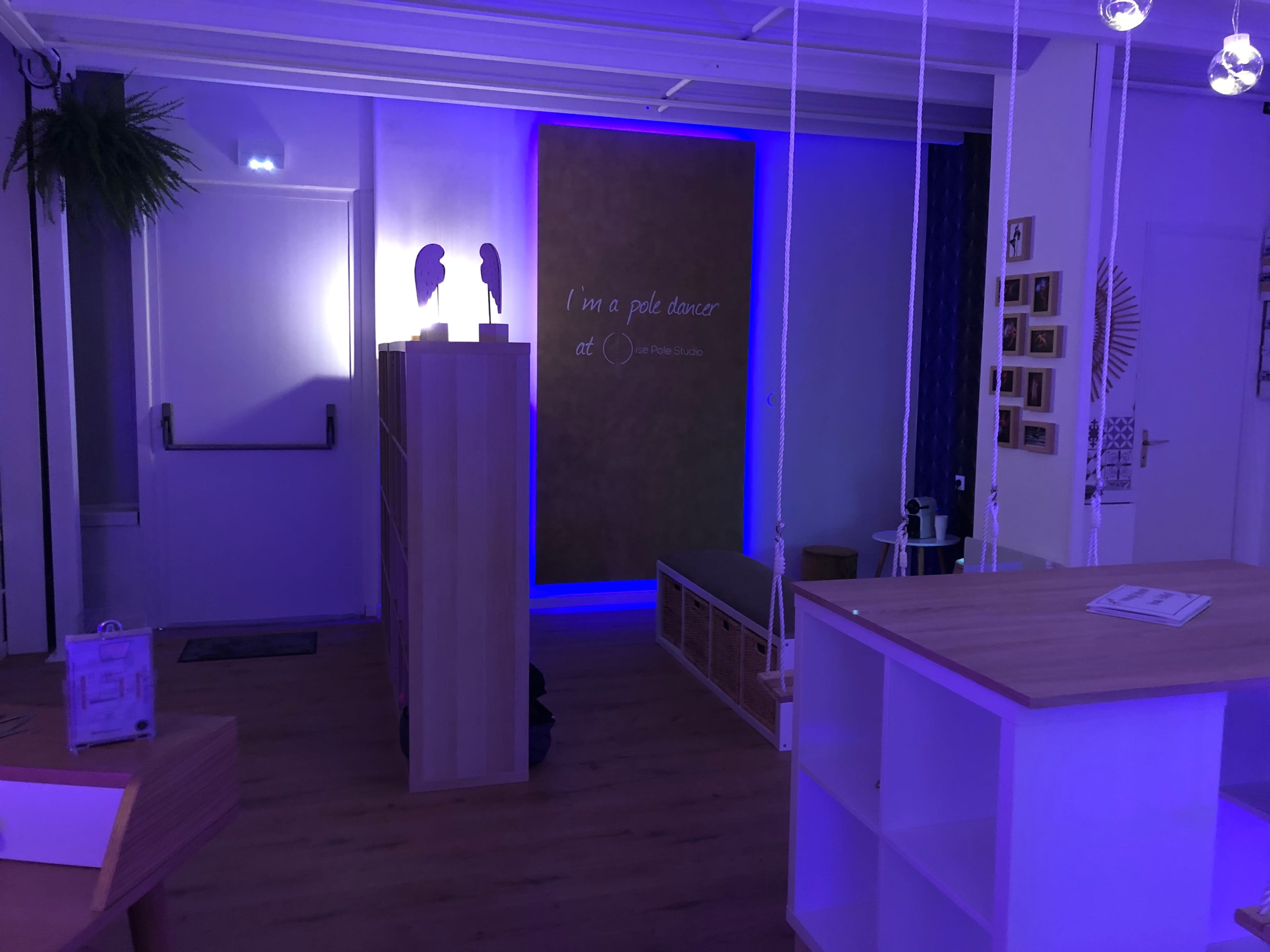 A brightly lit room with wooden furniture and a wall displaying the phrase "I'm a pole dancer" illuminated by purple lighting.