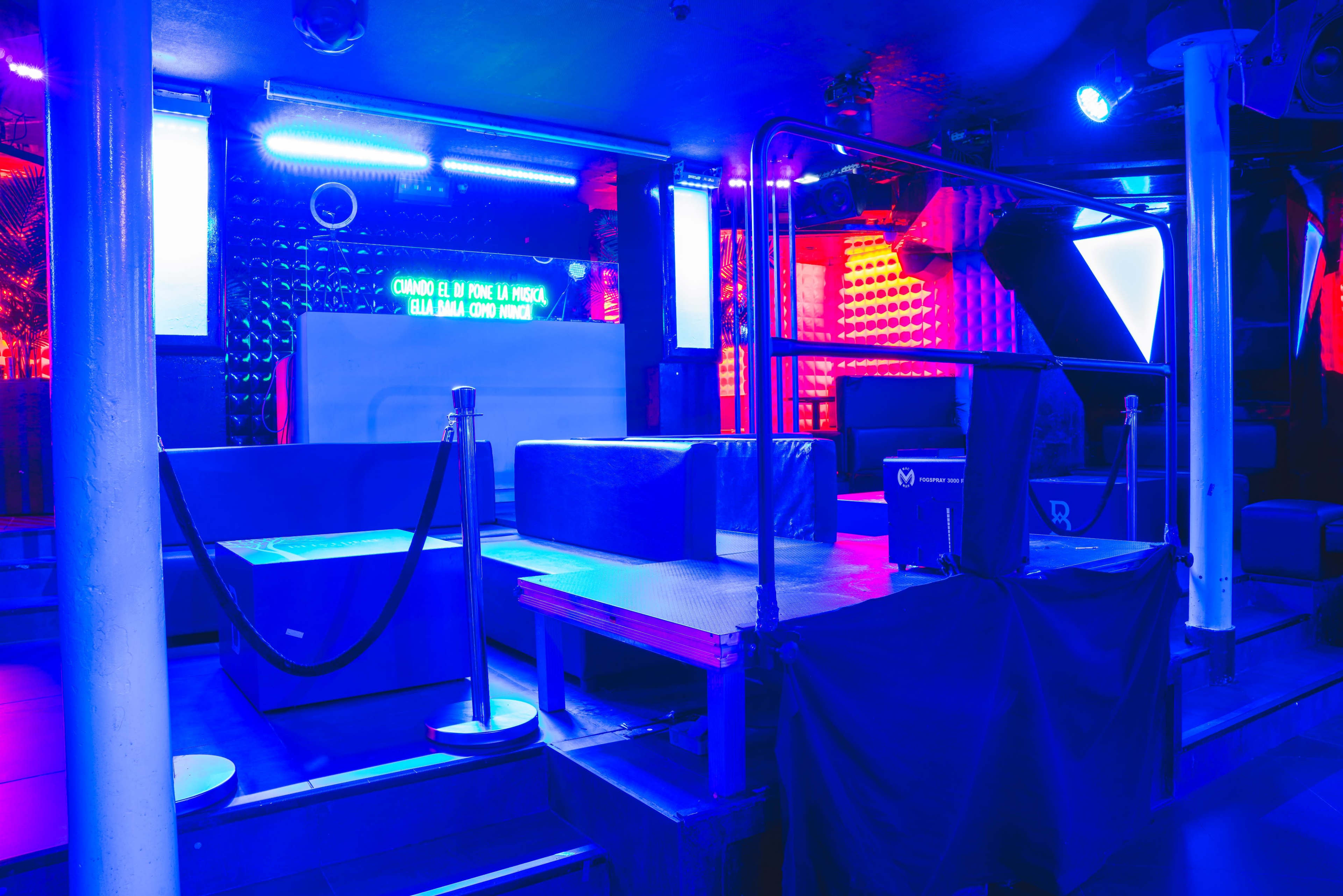 The image shows a dimly lit nightclub interior with illuminated seating areas and a stage for performances.
