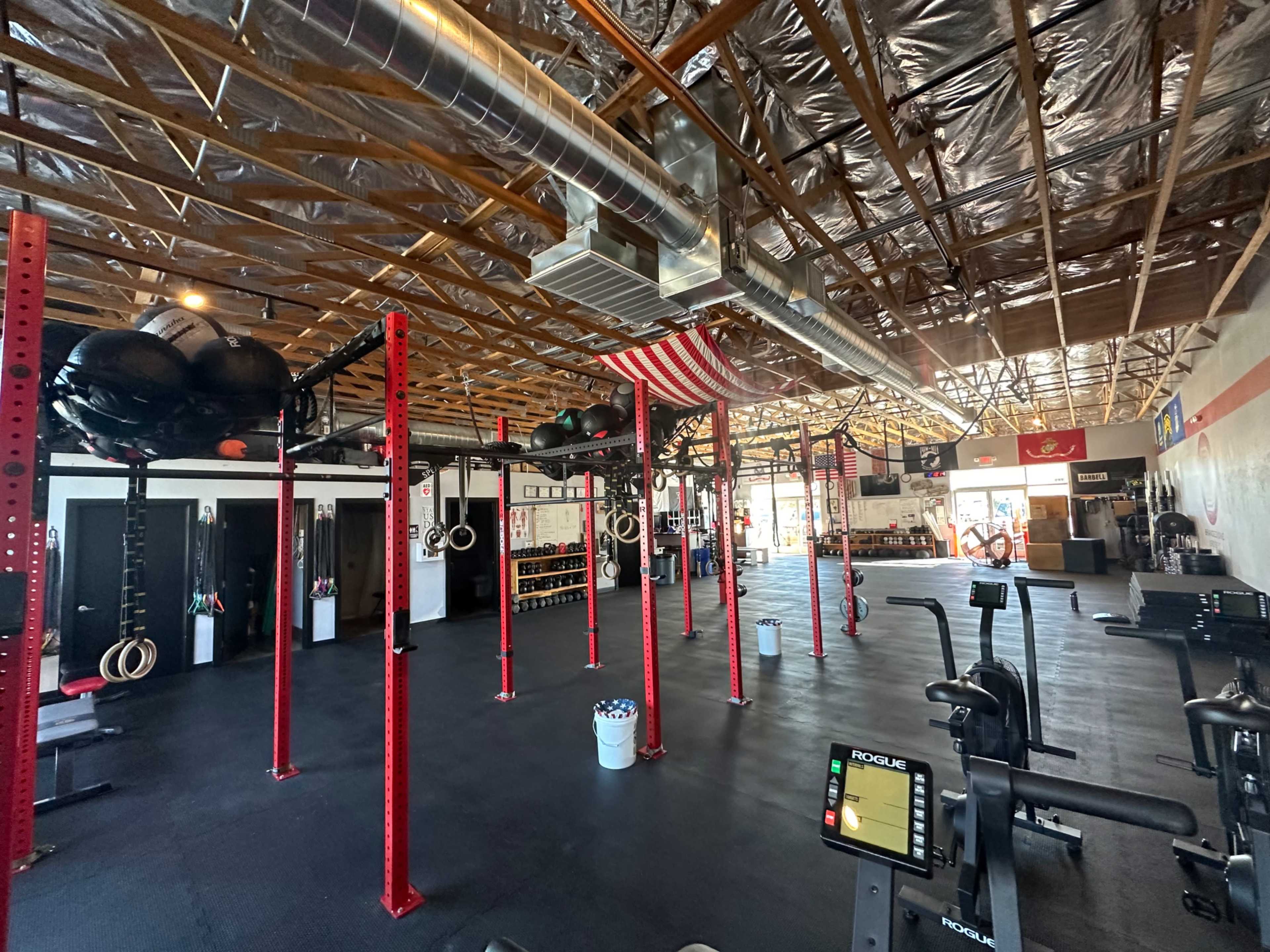 The interior of a gym with red weightlifting racks, exercise equipment, and an American flag hanging from the ceiling.