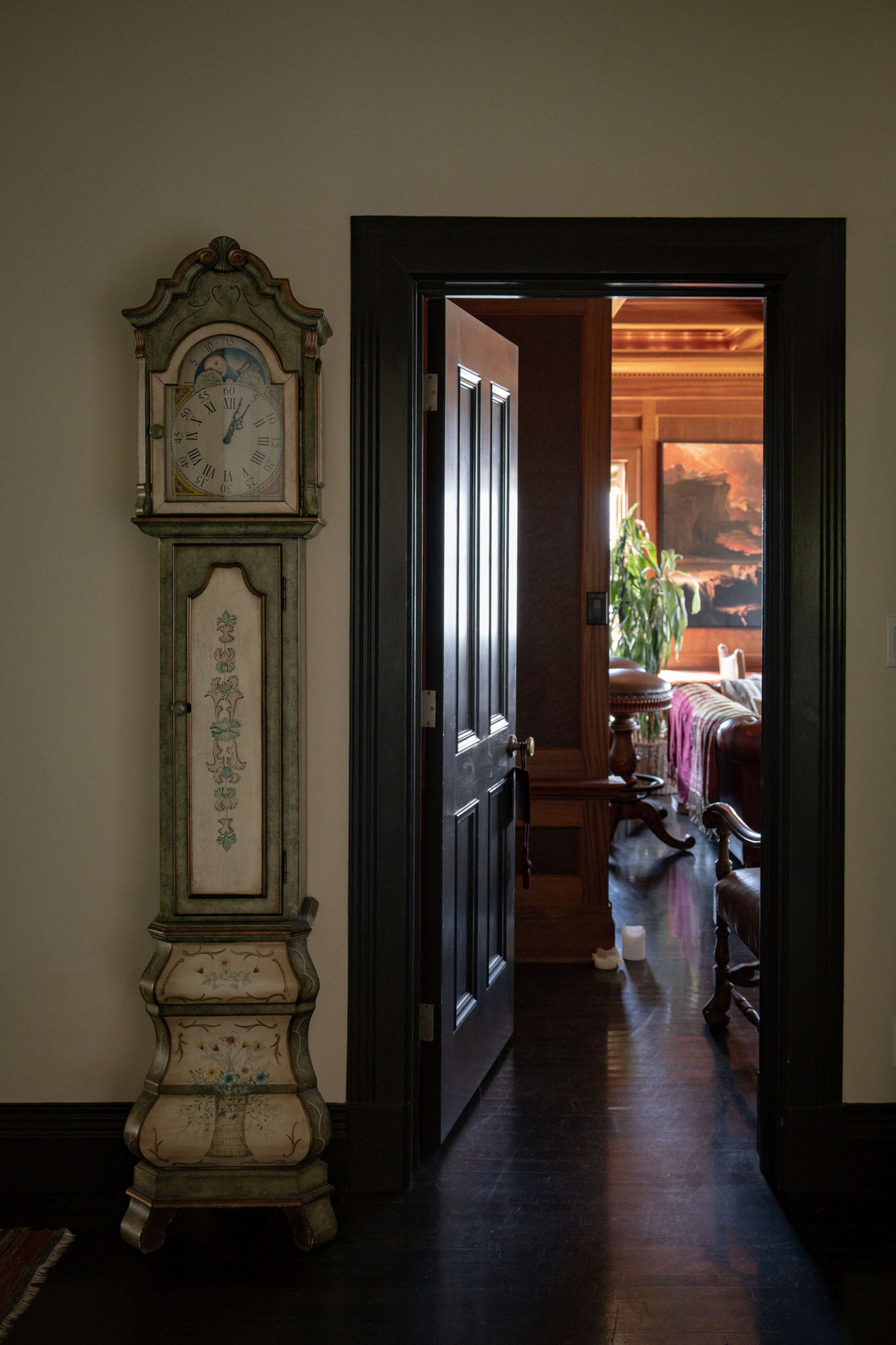 A tall, antique clock stands against a wall next to an open door leading to another room.