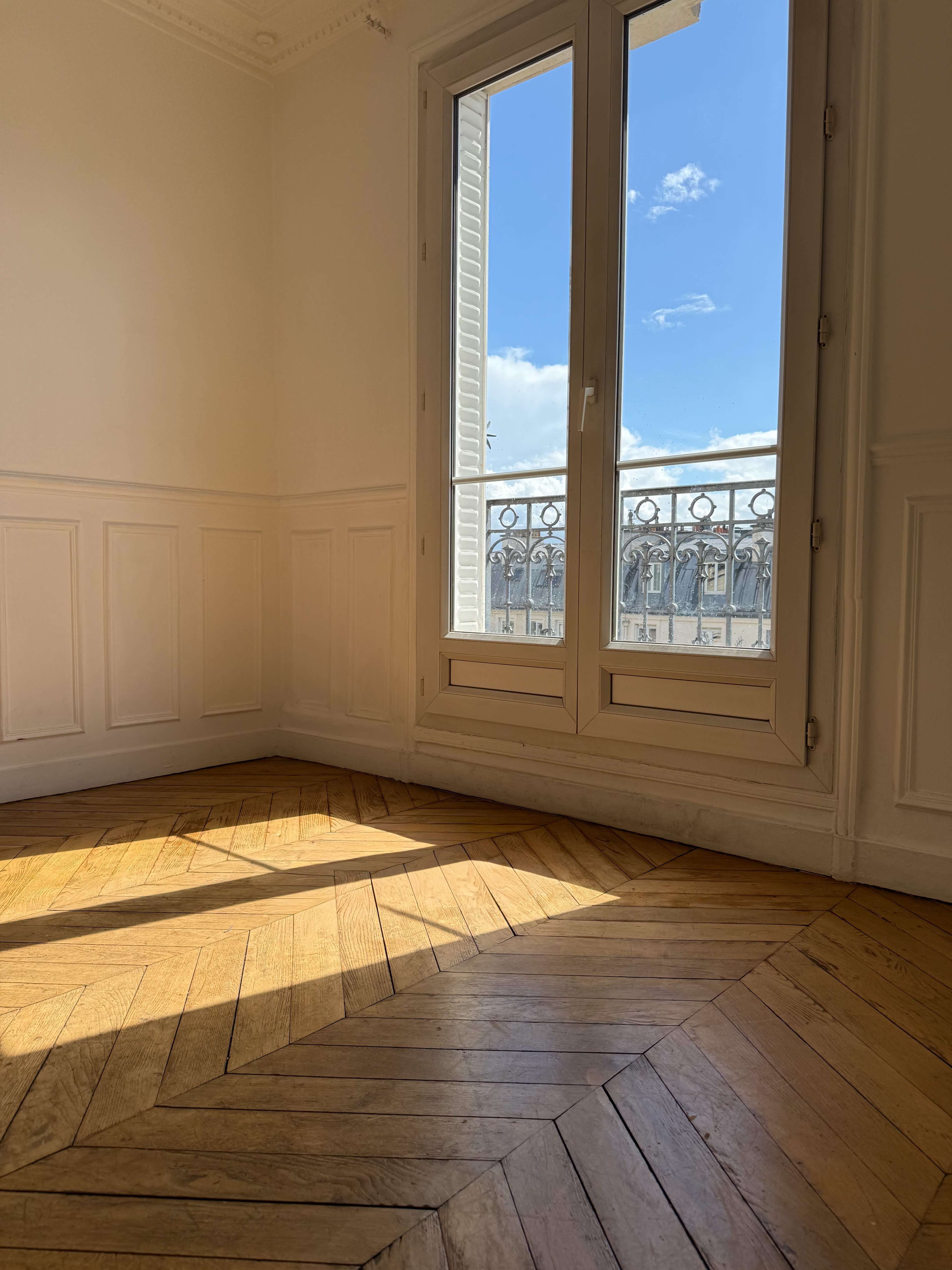 Sunlight streams through a large window, illuminating the parquet floor in a corner of a room.