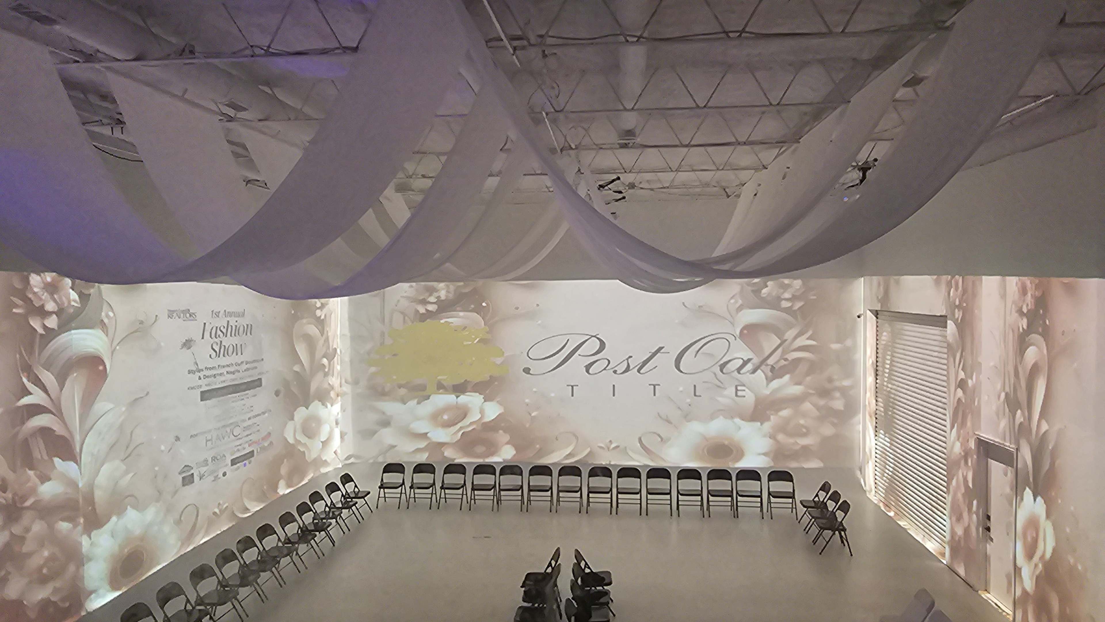 The image shows a spacious event venue with projecting floral designs on the walls and a circle of empty chairs arranged in the center.