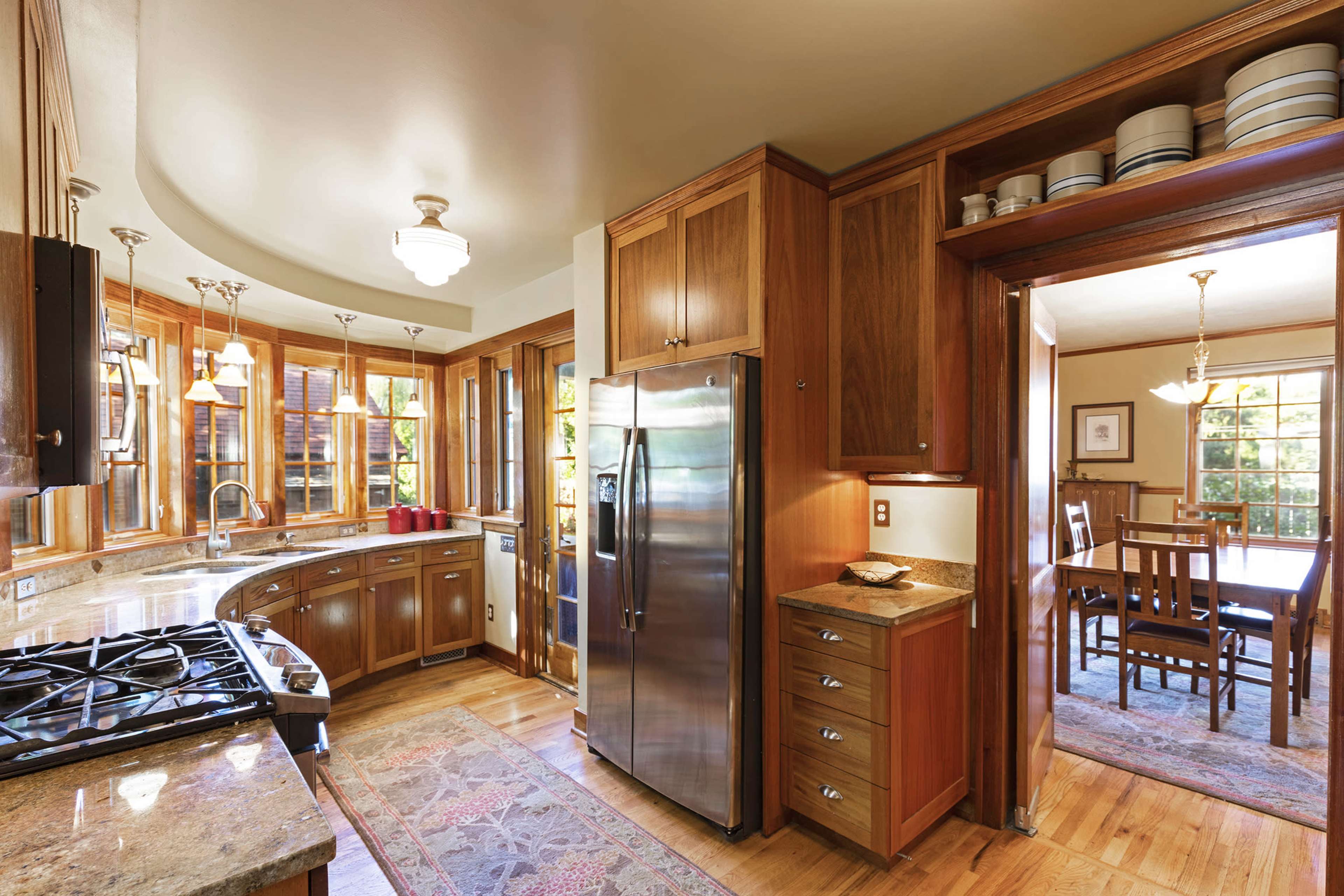 A modern kitchen features wooden cabinetry, stainless steel appliances, and a view of an adjoining dining area through large windows.