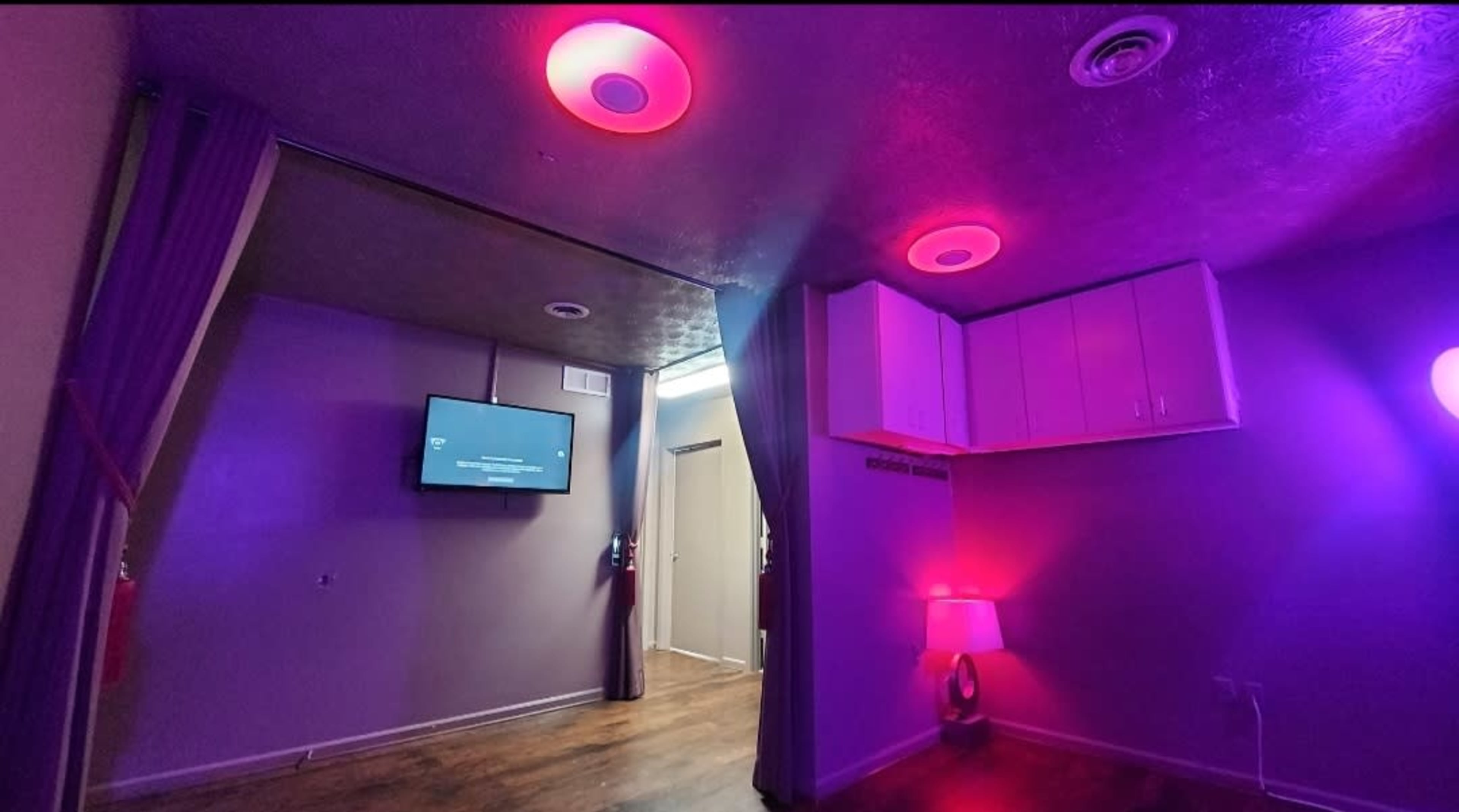 The image shows a room with purple and pink lighting, a television mounted on the wall, and a doorway leading to another space.