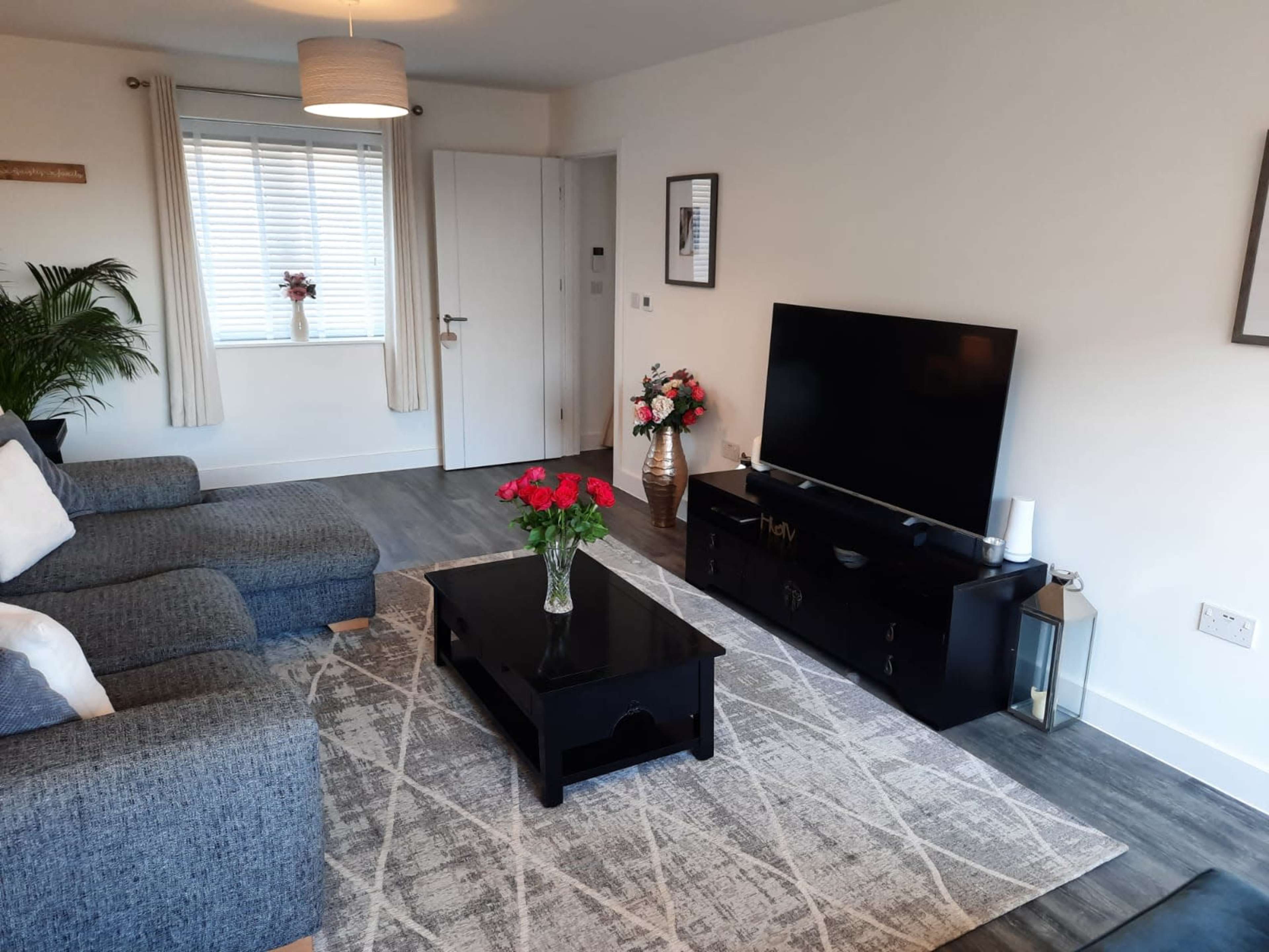 A modern living room with a gray sofa, a coffee table, a large television, and decorative flowers on a table.
