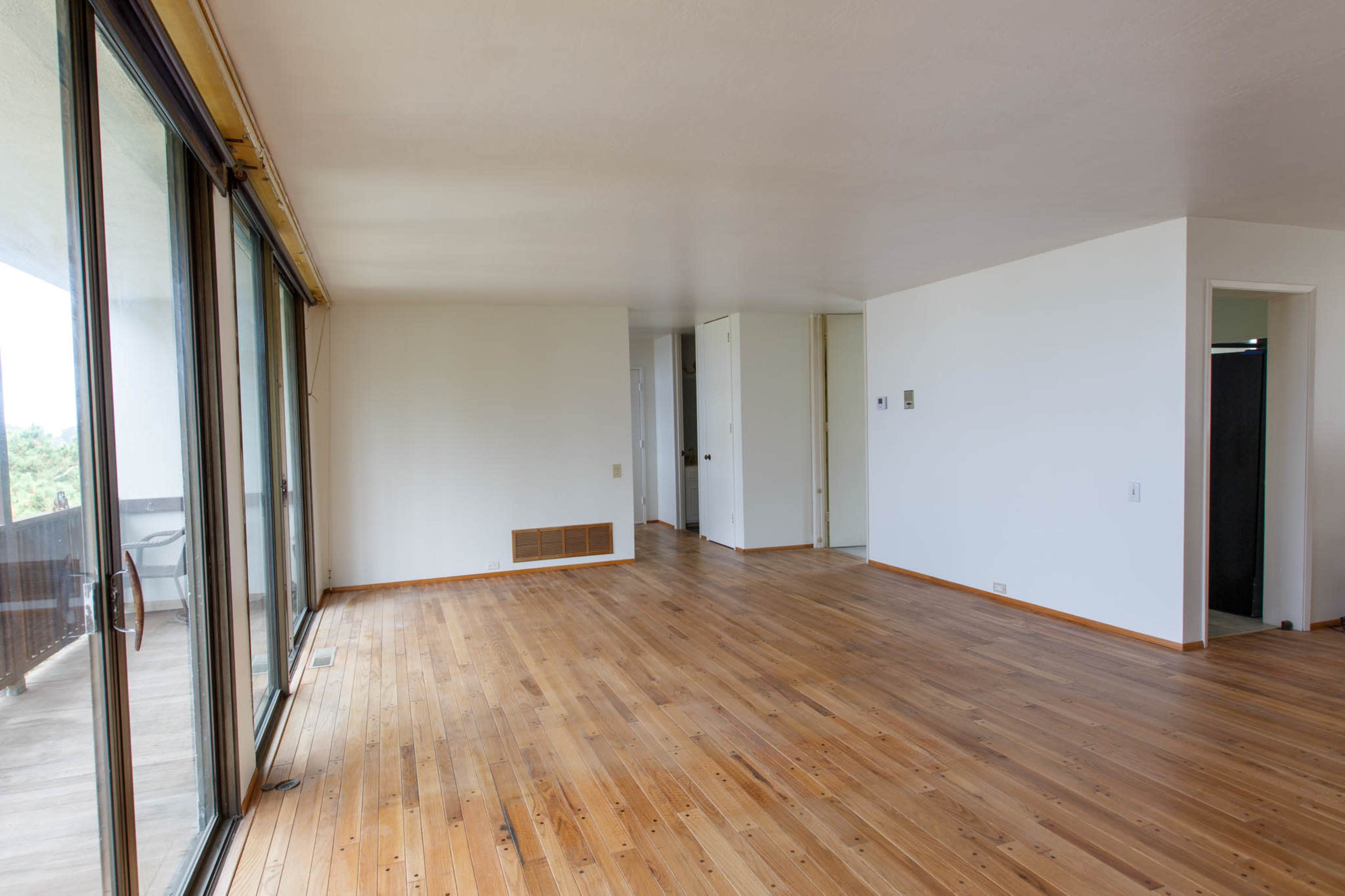A spacious, empty room with hardwood flooring and large windows overlooking a balcony.