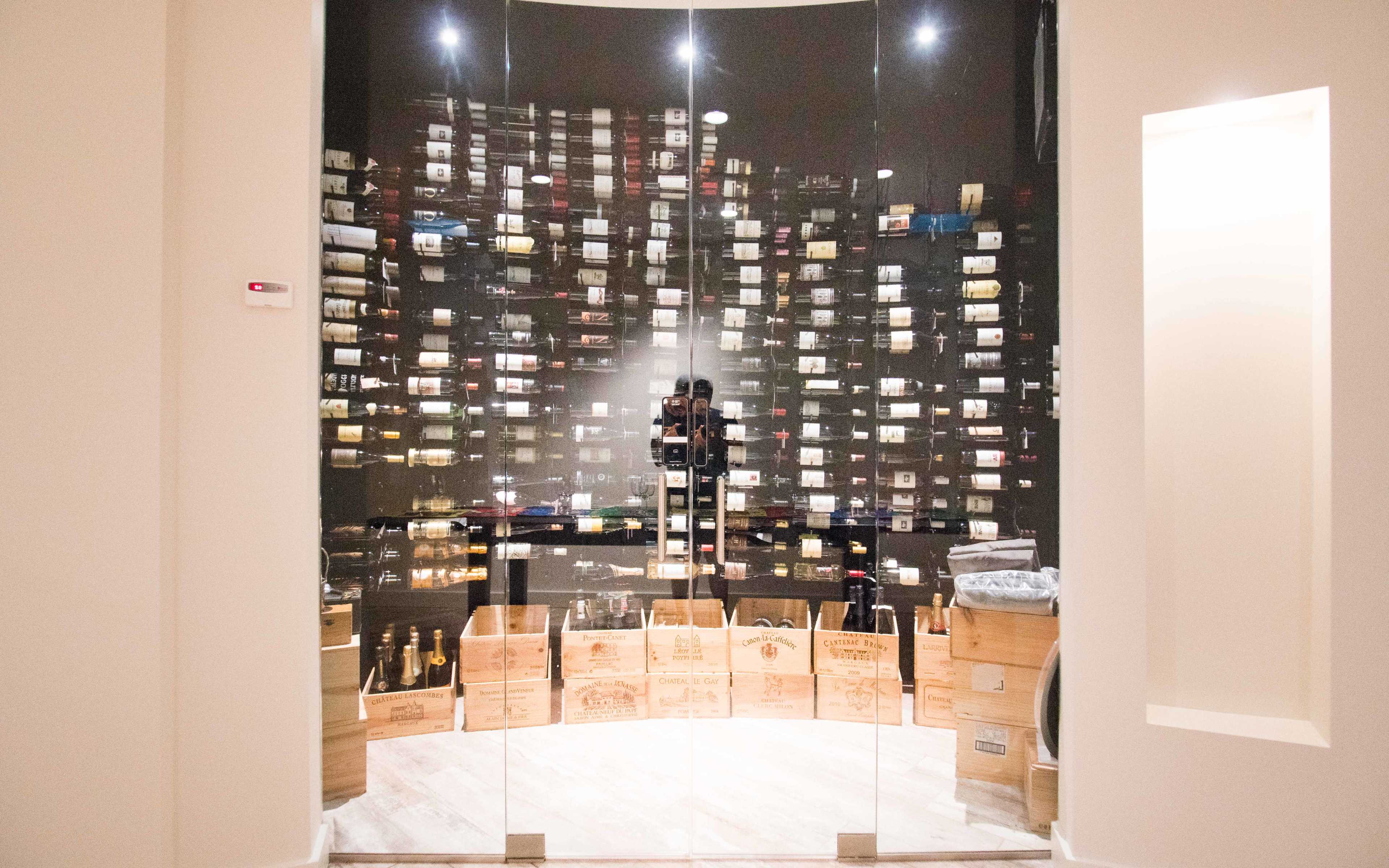 A glass wine cellar featuring neatly arranged bottles on shelves, with wooden crates at the bottom.