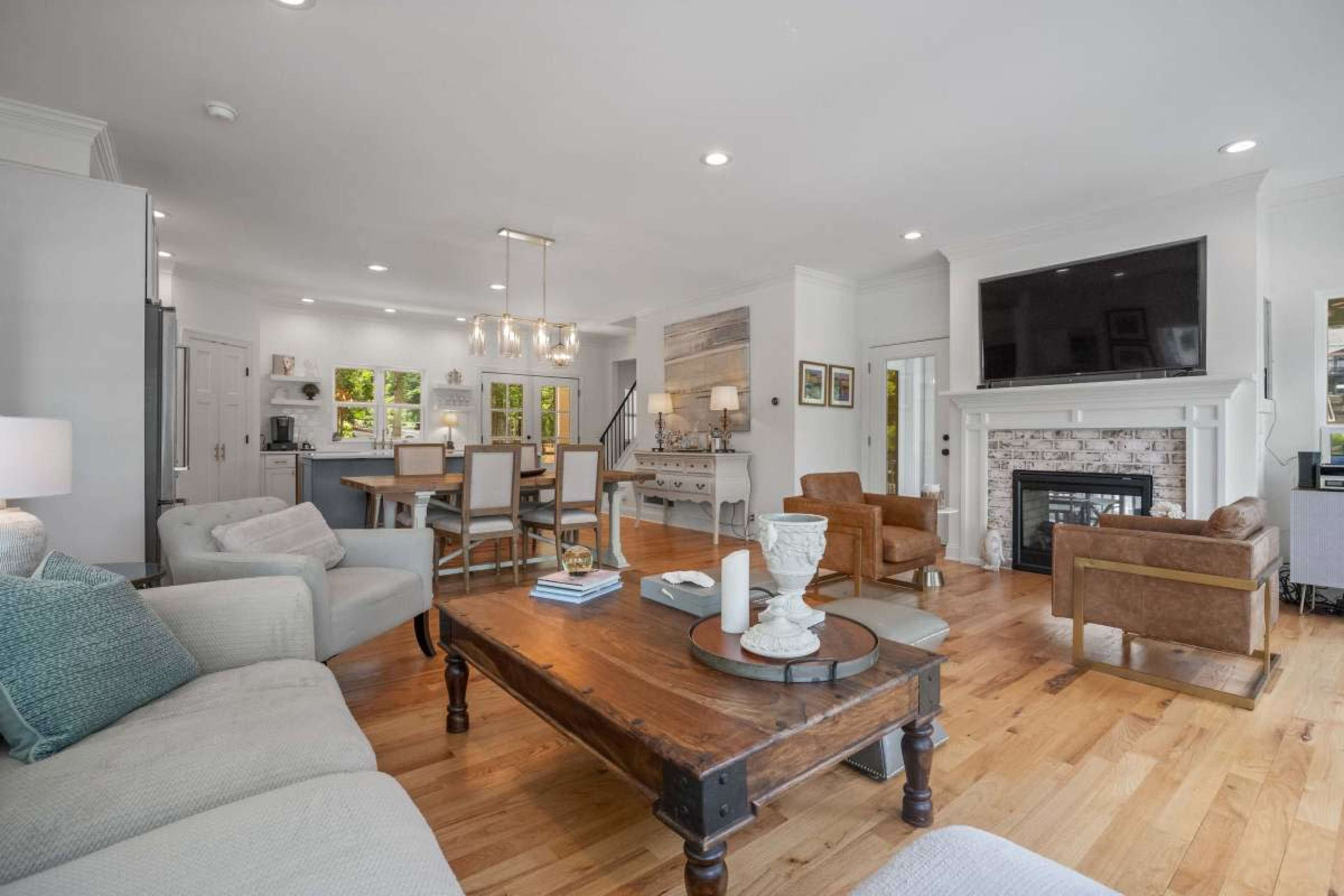 The image shows a modern living room and dining area with hardwood floors, a large coffee table, a fireplace, and seating arrangements.
