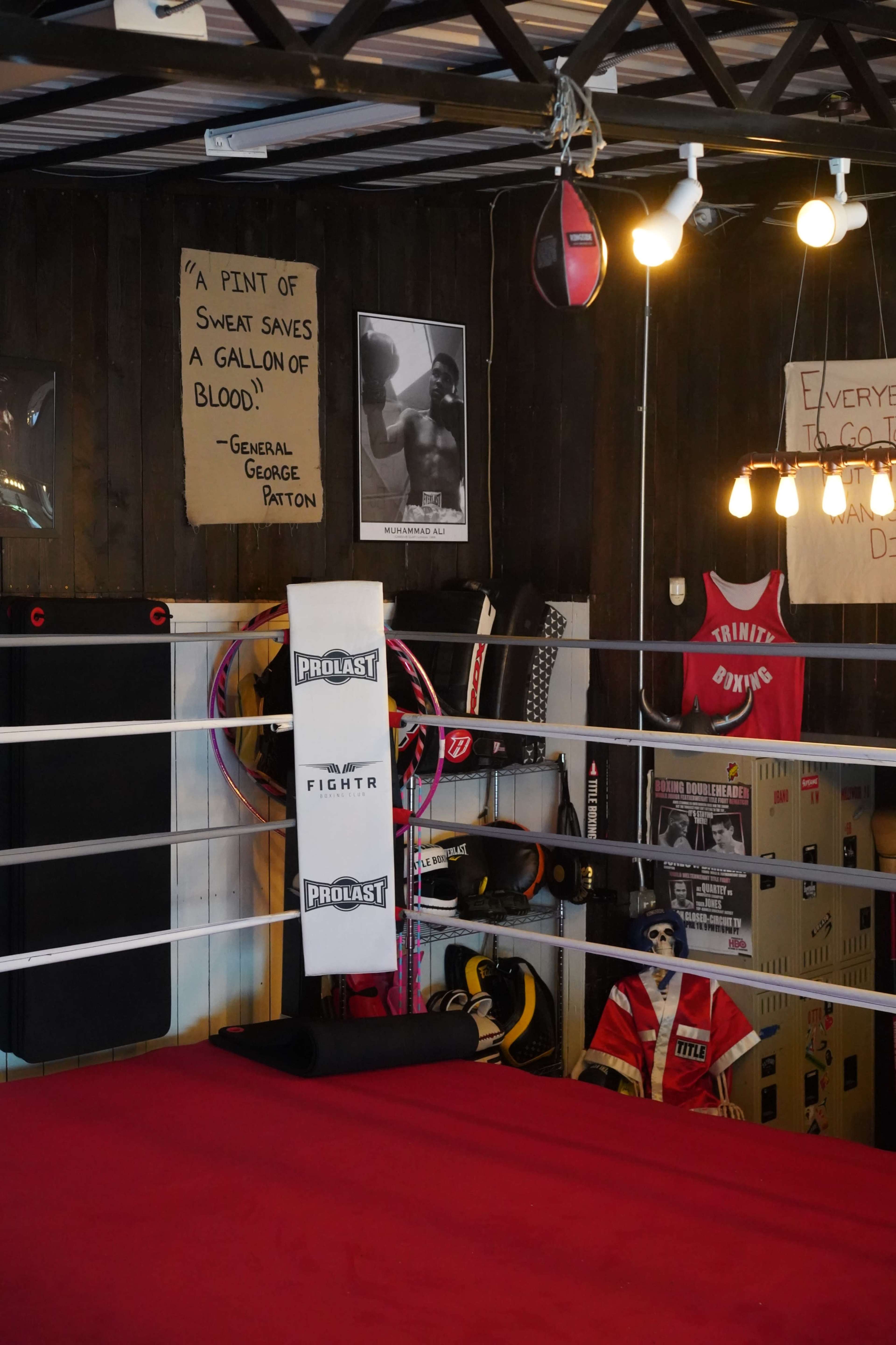 A boxing gym with a red boxing ring, hanging punching bags, and various training equipment along the walls, adorned with motivational posters.