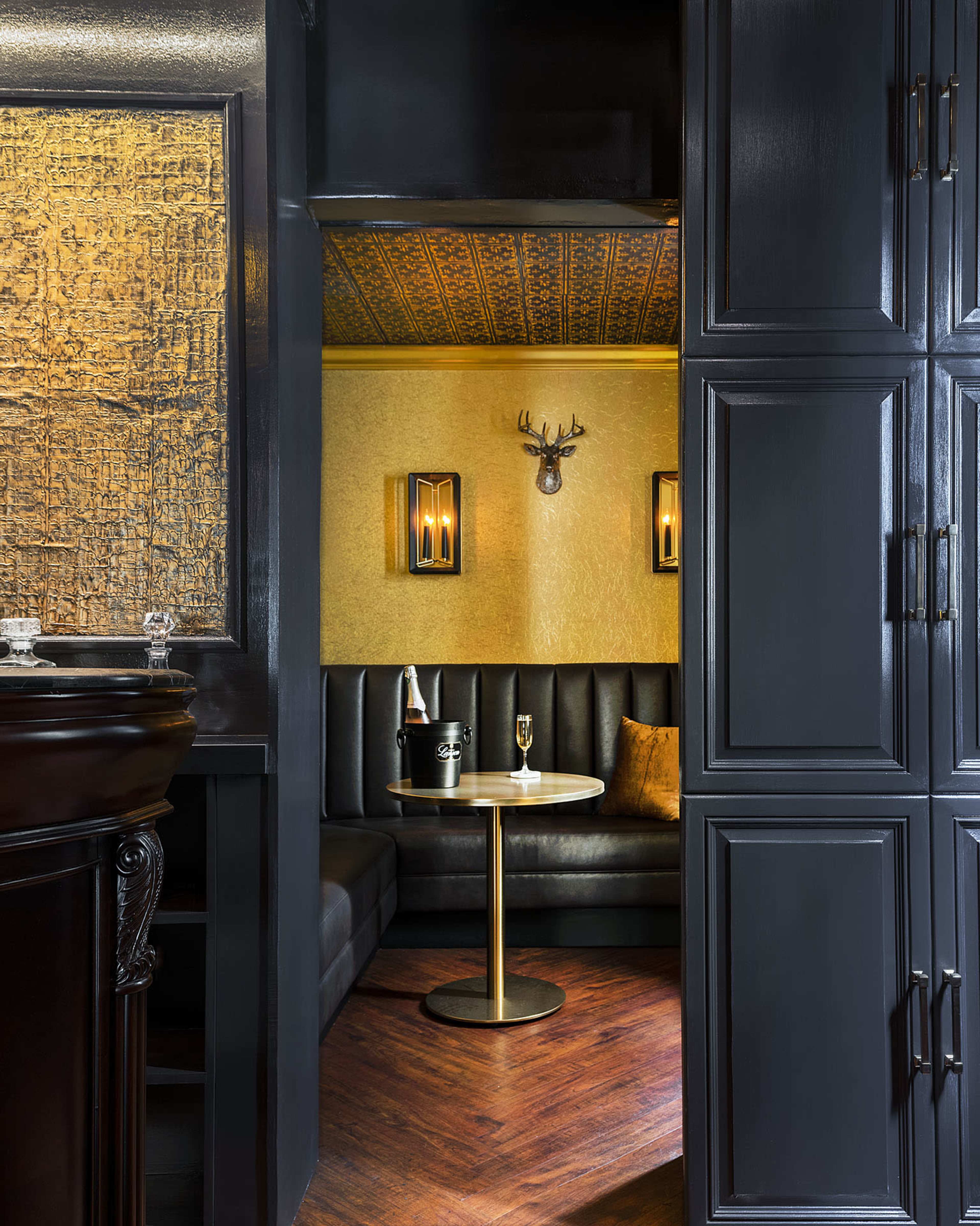 A cozy, dimly lit lounge area with a black leather couch, a round table, and decorative wall sconces.
