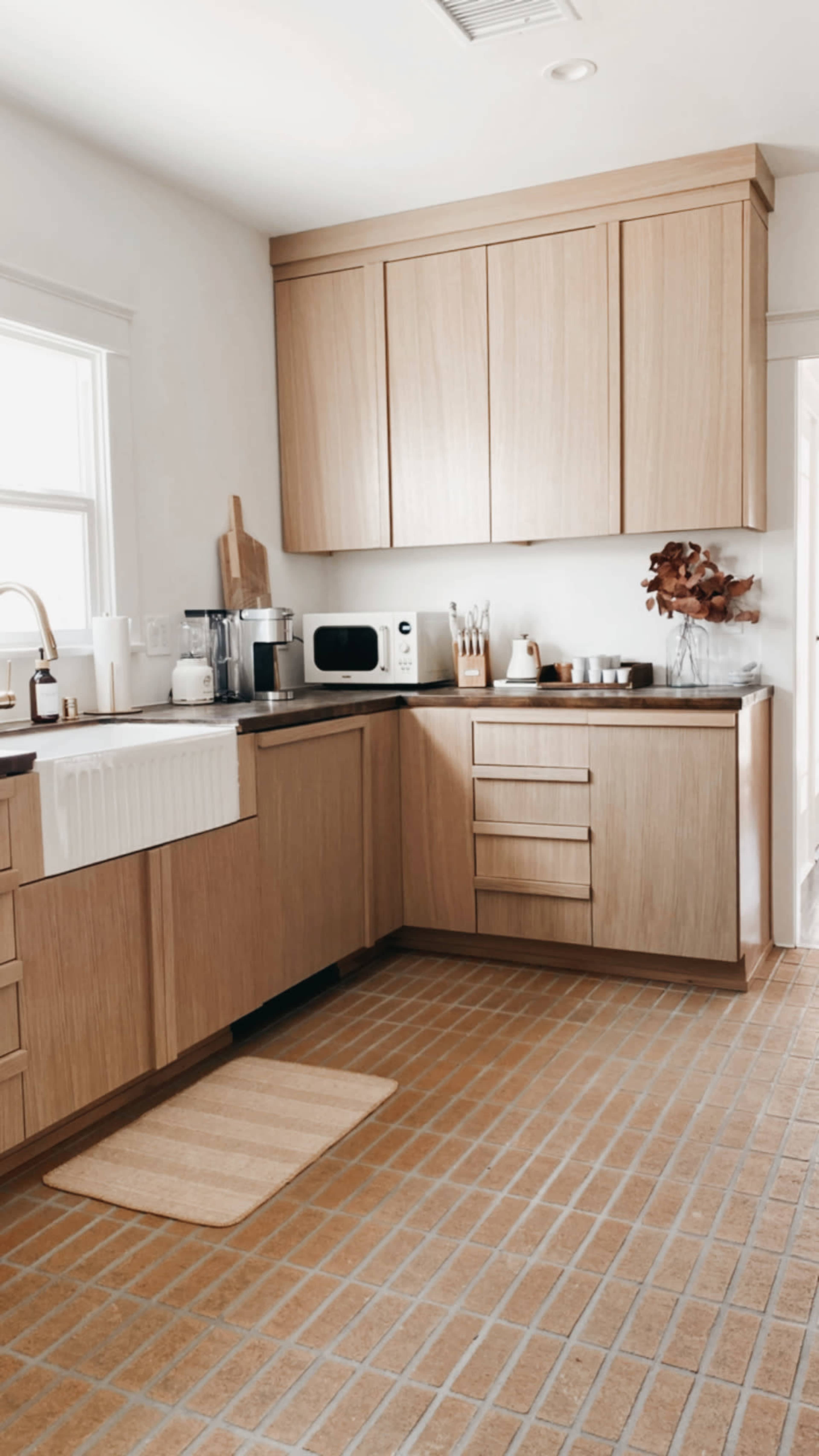 A modern kitchen features wooden cabinetry, a farmhouse sink, a microwave, and a tiled floor.