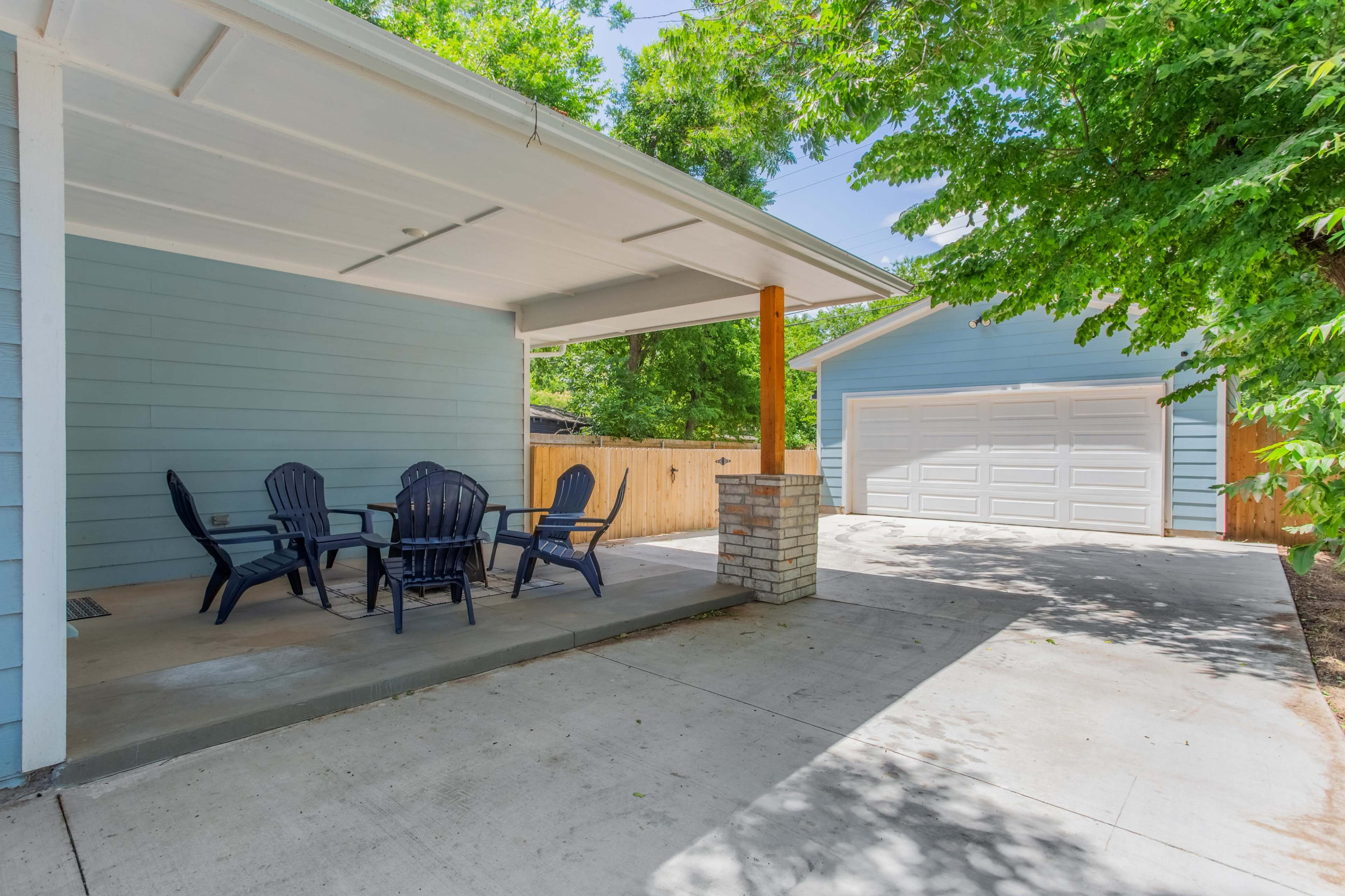 A patio with black outdoor furniture is situated next to a driveway leading to a two-car garage.