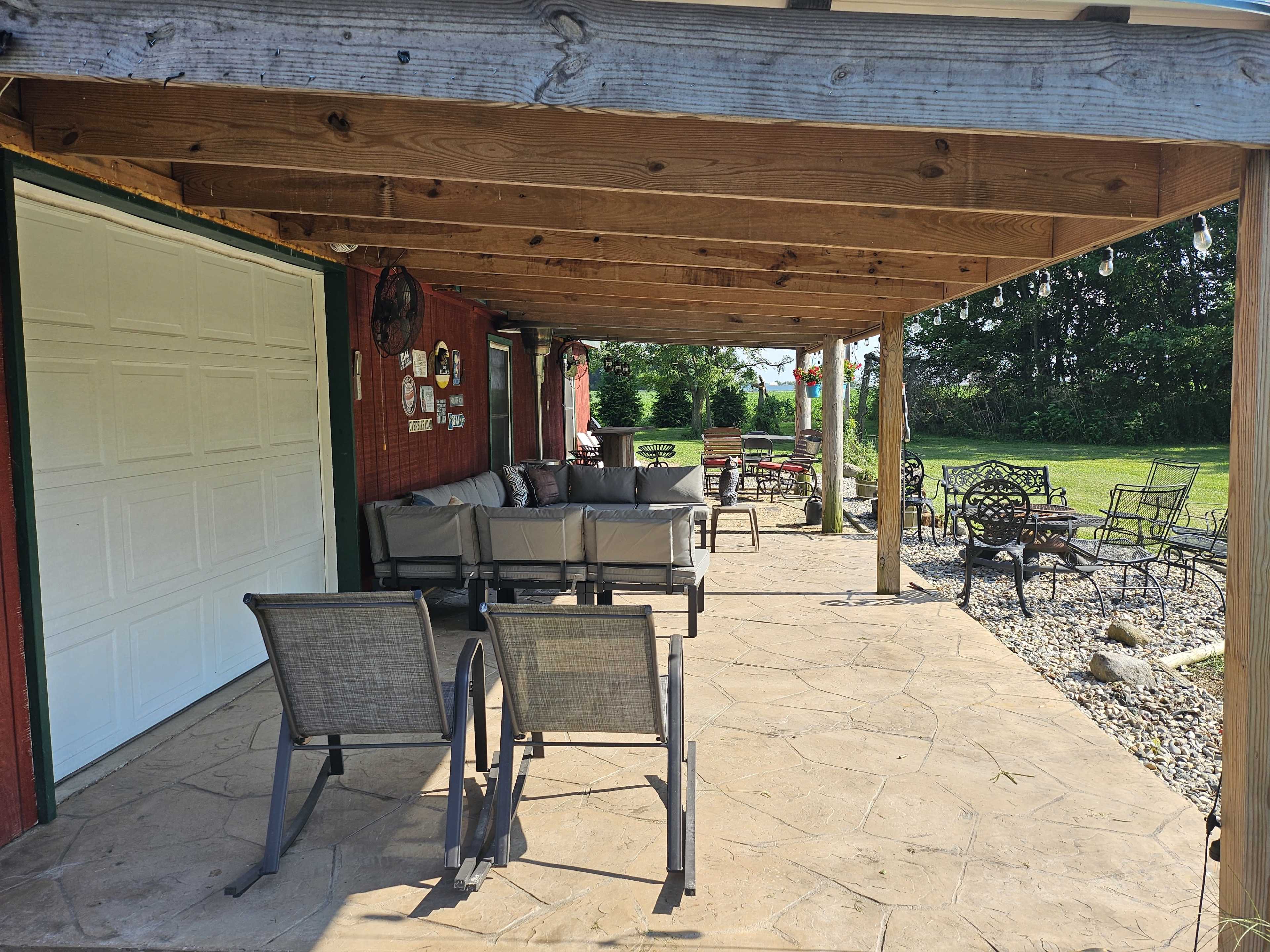A covered patio area with seating, a stone floor, and a lawn in the background.