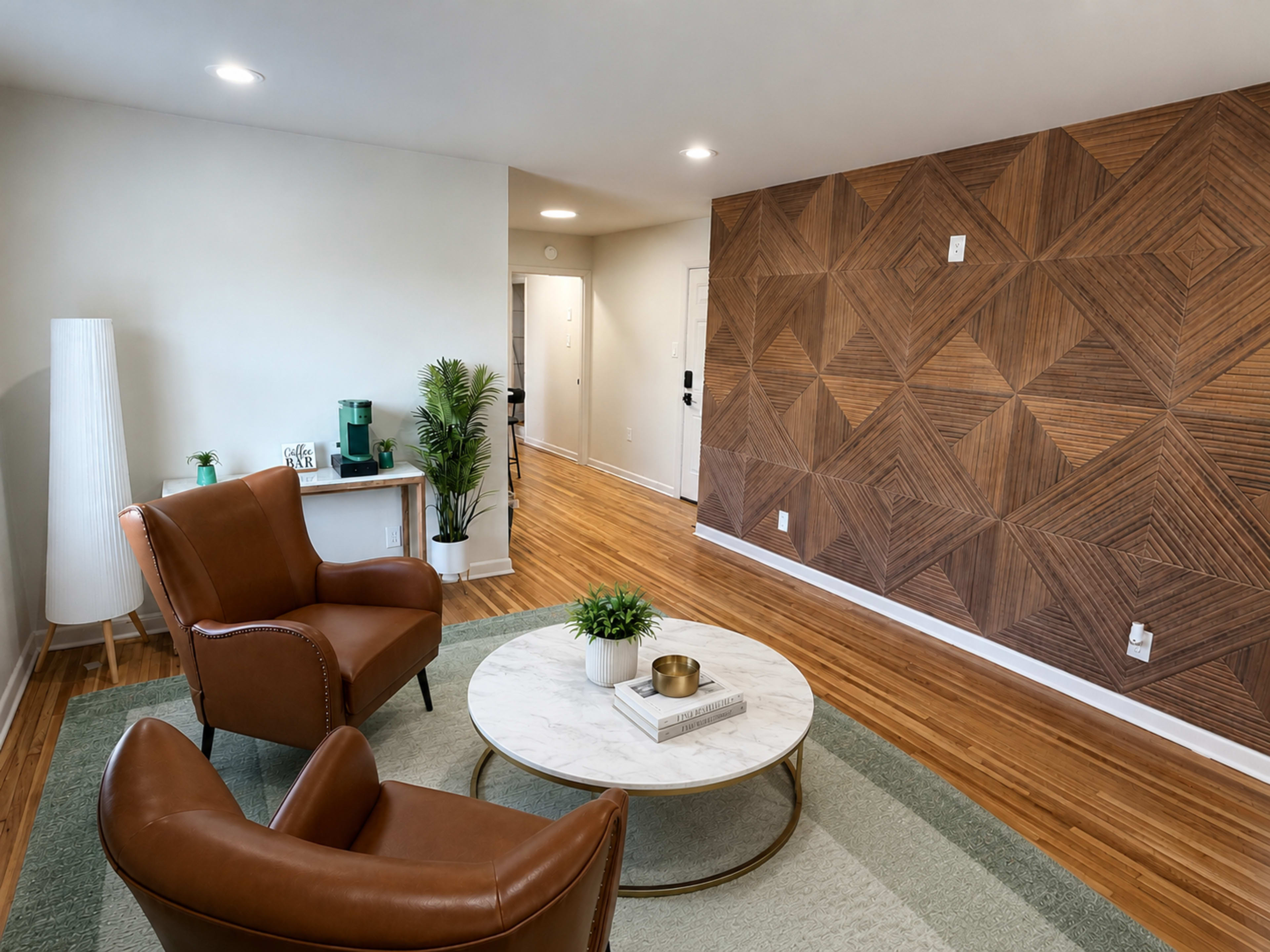 The image features a modern living room with two brown leather chairs, a round marble coffee table, and a patterned wooden accent wall.