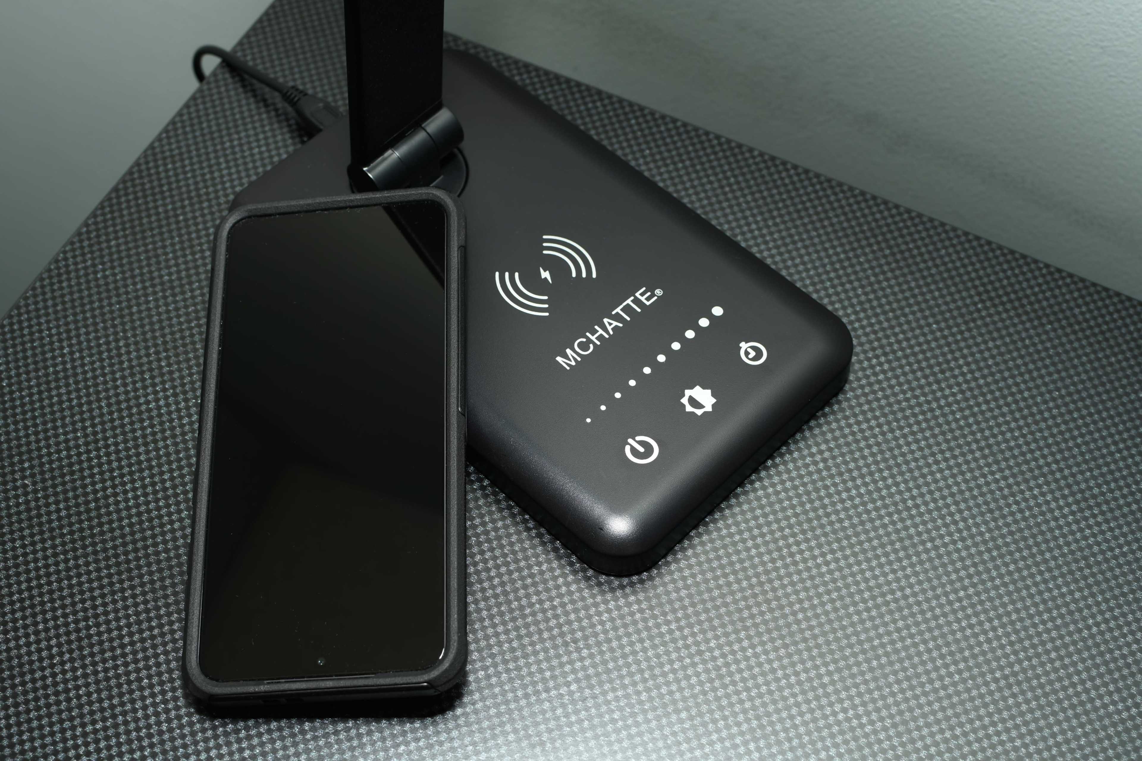 A smartphone rests next to a wireless charging pad on a textured surface.