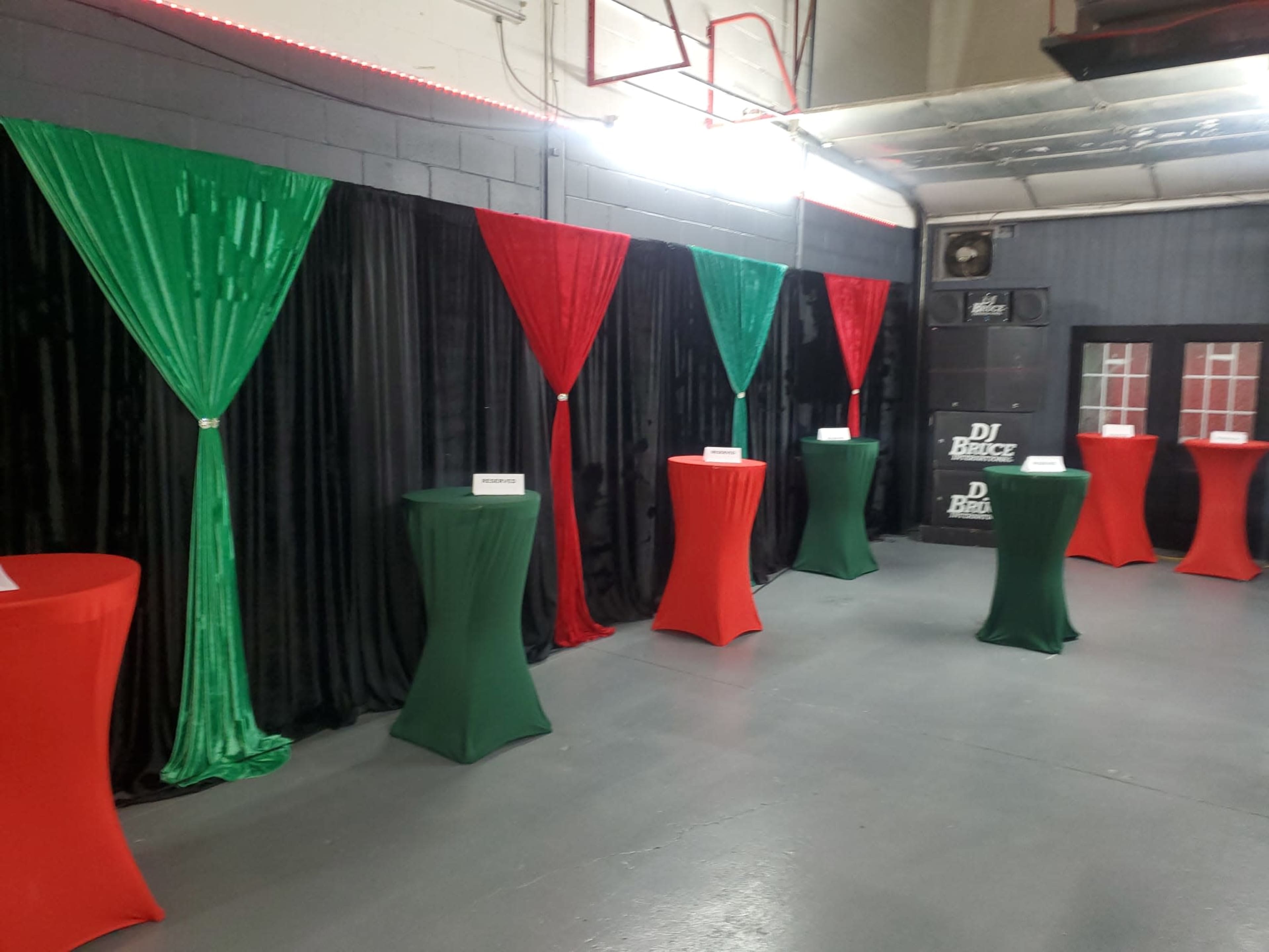 The image shows a room with black walls adorned with red and green drapes, and several round tables covered in red and green tablecloths.