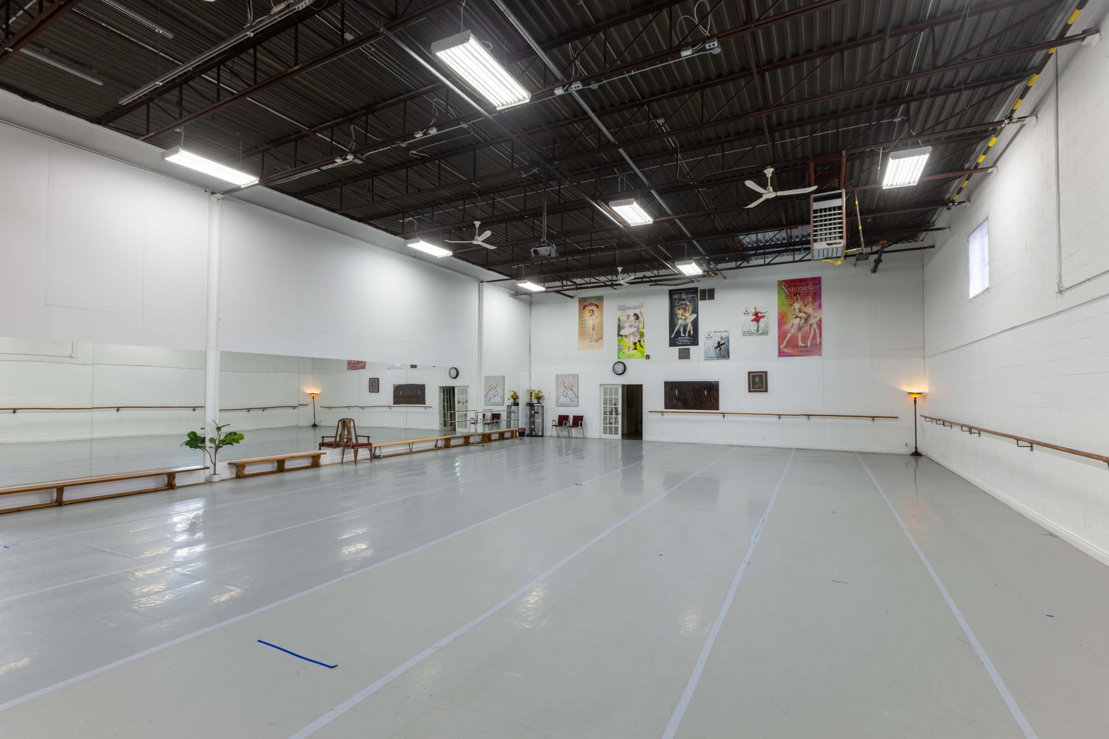 The image shows a spacious dance studio with mirrored walls, wooden ballet barres, and various artworks displayed on the walls.