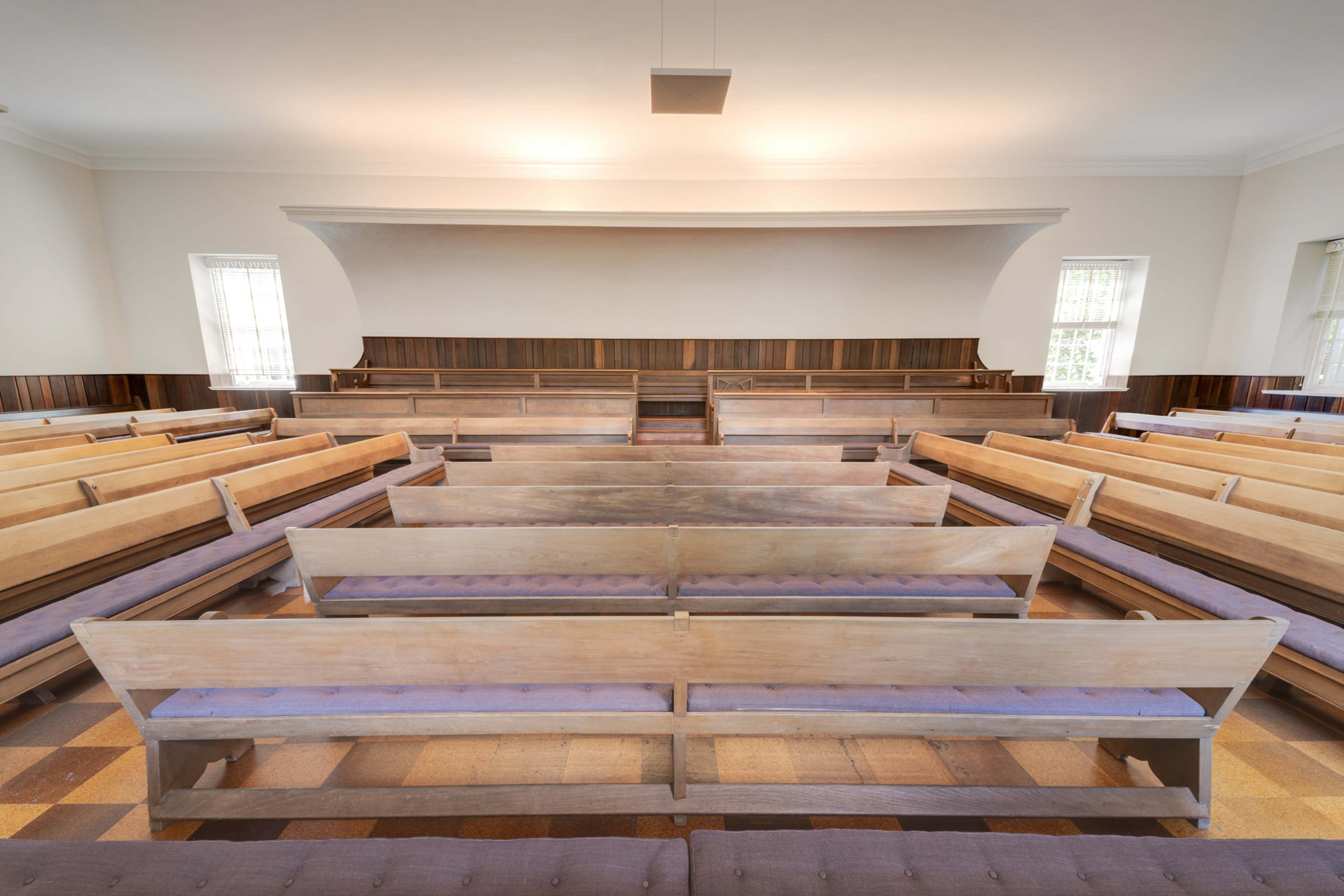 A simple interior of a church with wooden benches arranged in rows facing a central podium.