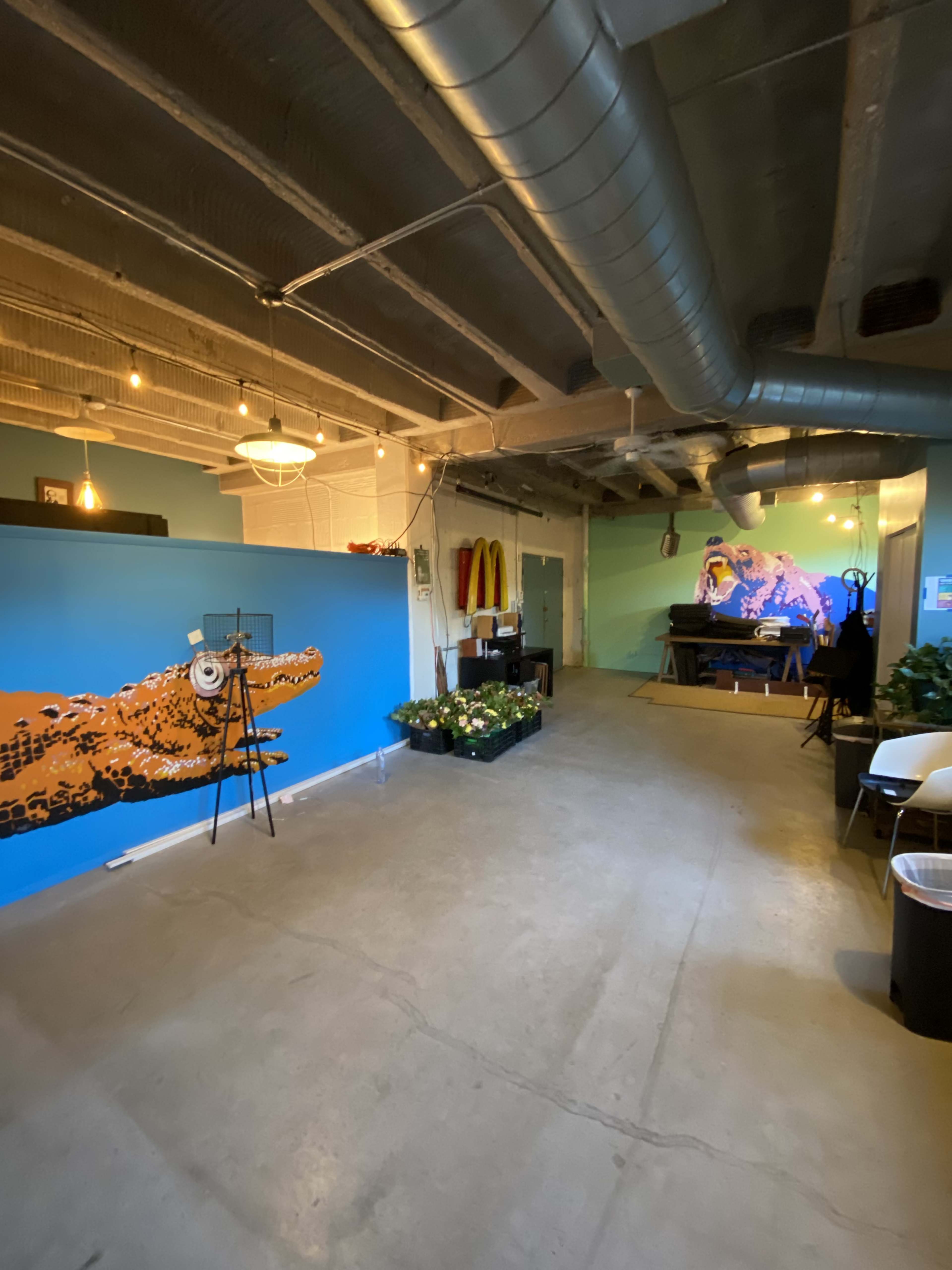 An industrial-style room with a blue-painted wall featuring an artistic mural, potted plants, and a workspace area with a table and chairs.