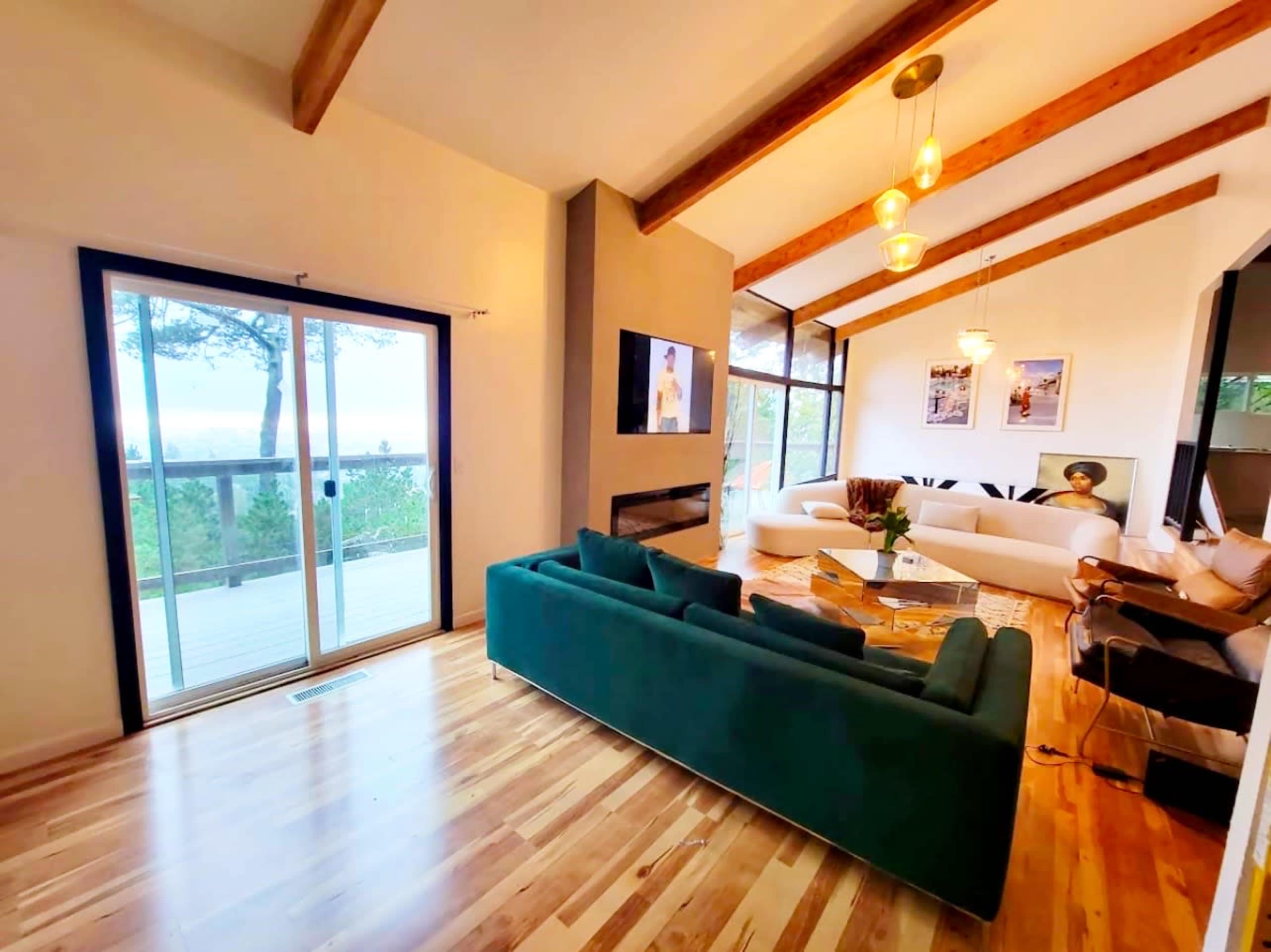 A spacious living room with a green sofa, wooden beams on the ceiling, and large windows that open to a view.