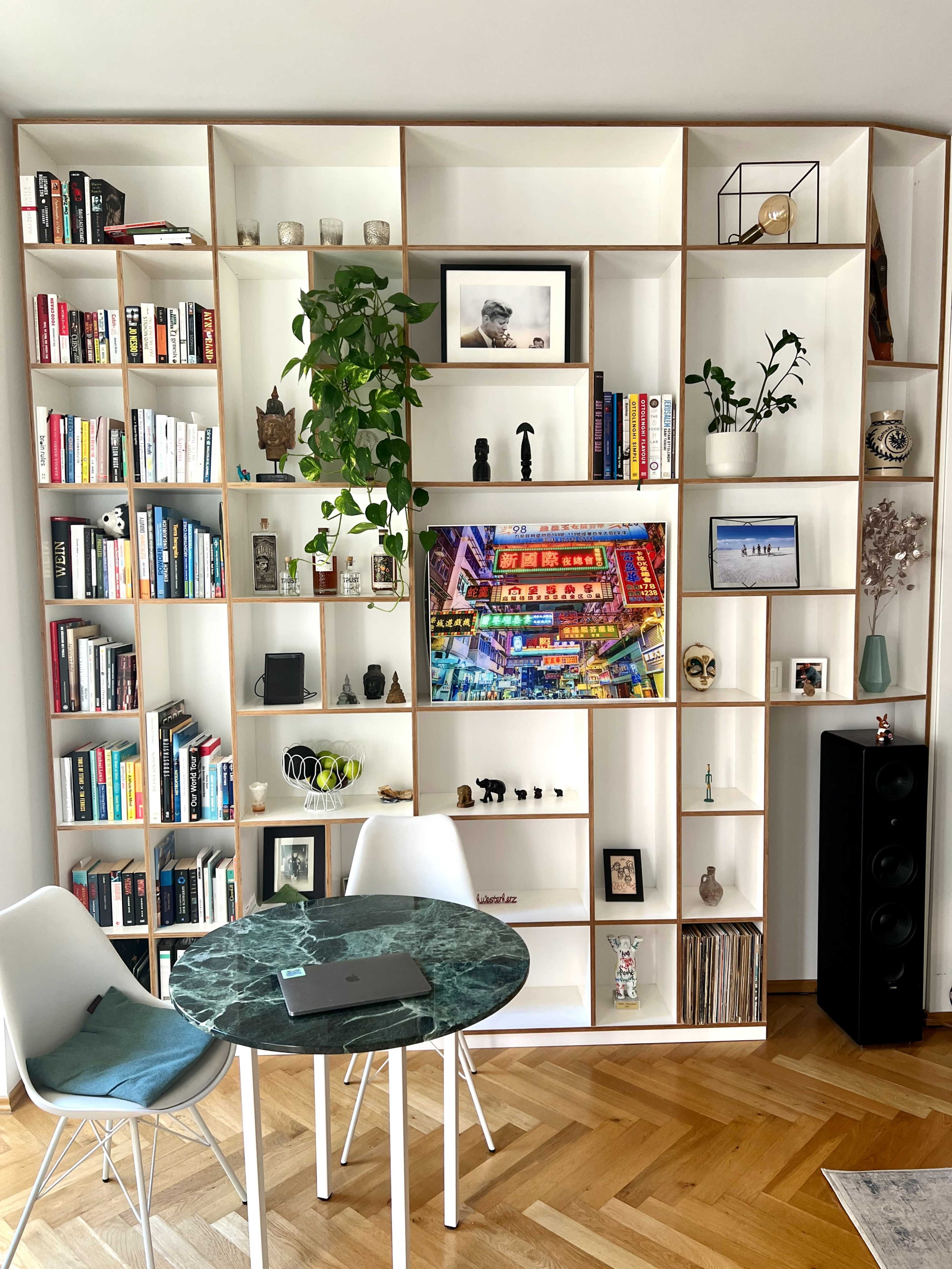 A modern bookshelf filled with books, plants, and decorative items, alongside a circular table with a marble top and electronic devices on it.