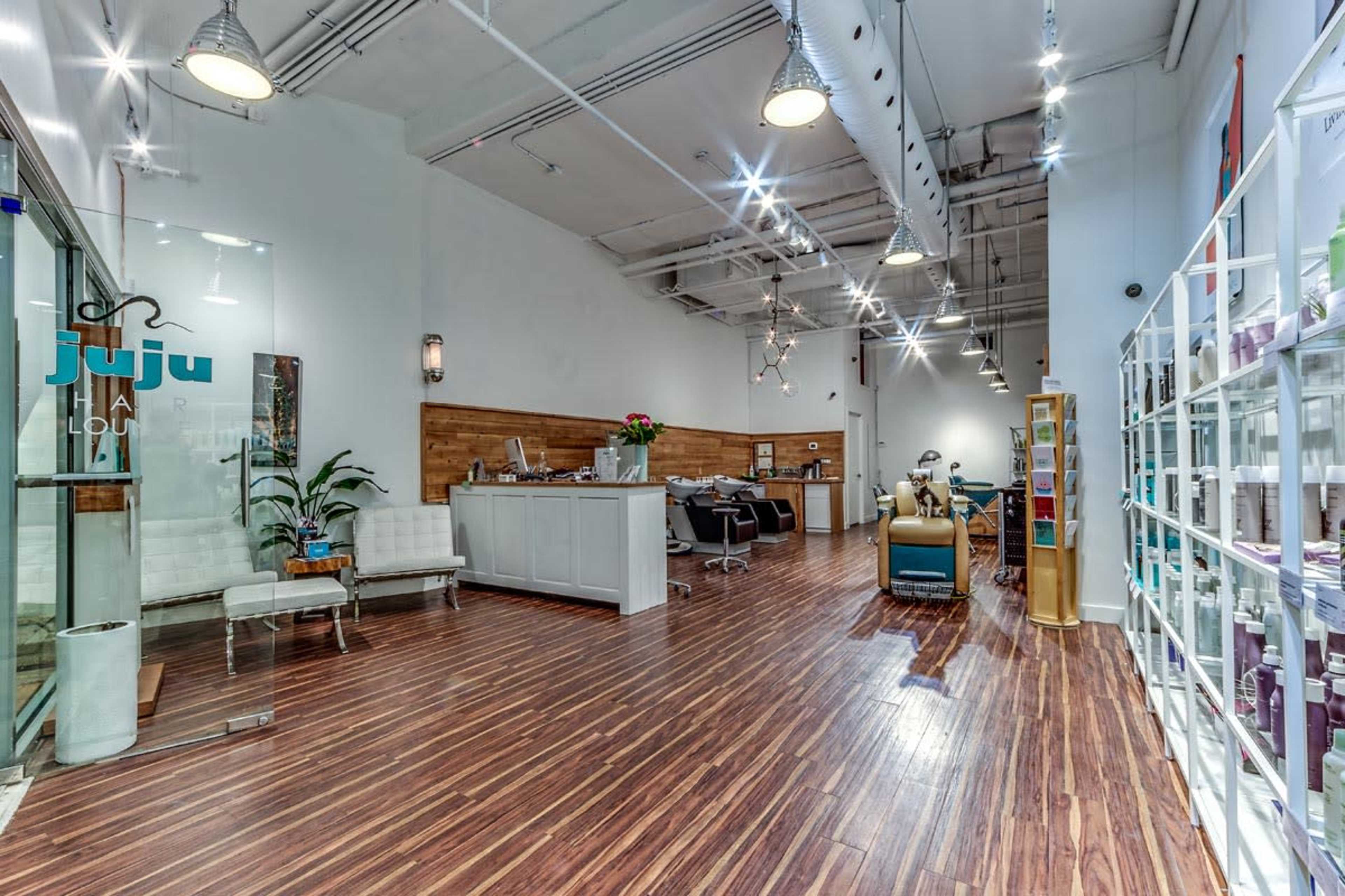 A modern salon interior with wood flooring, light-colored walls, a reception area, and styling stations.