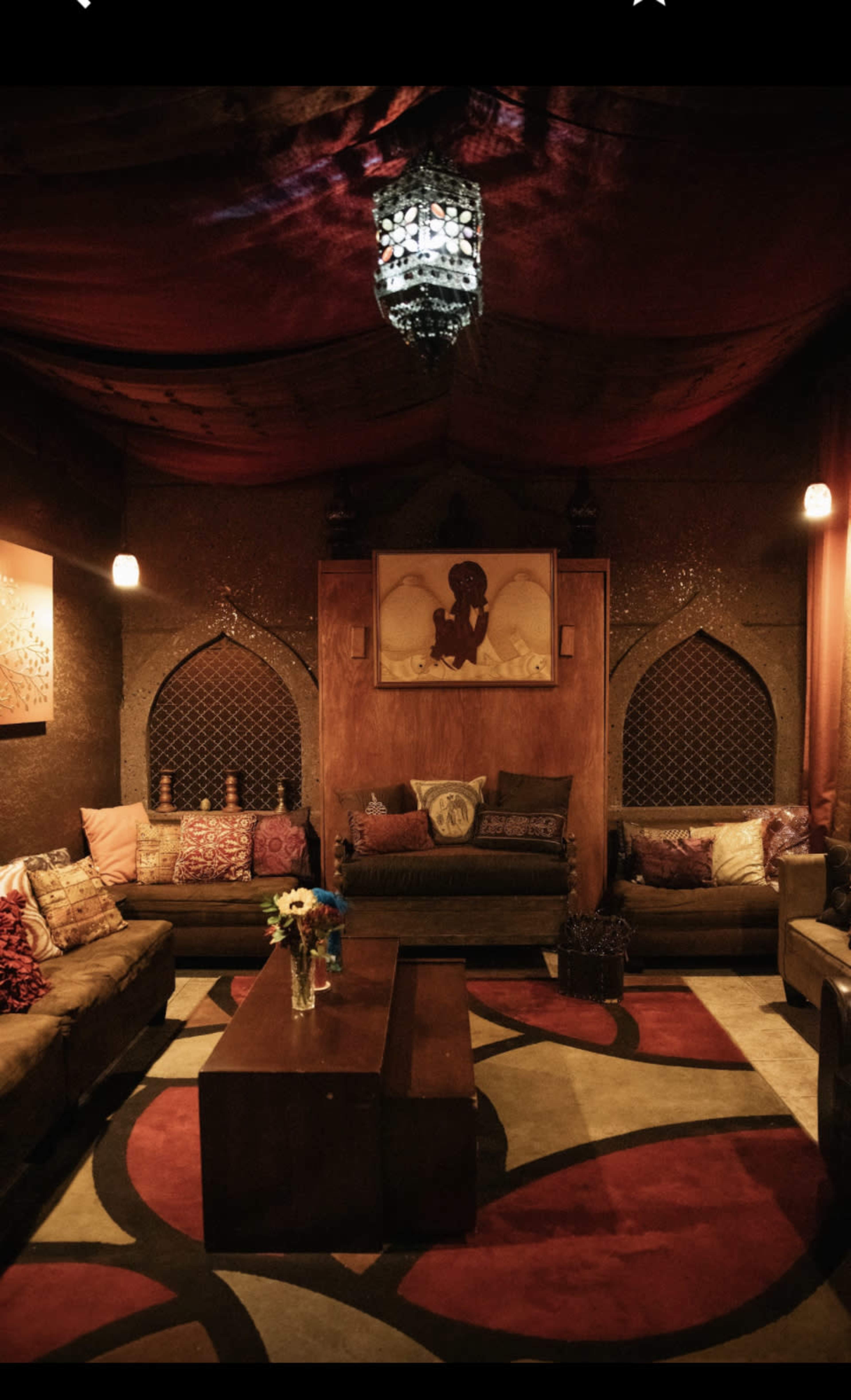 A cozy lounge area with low seating, decorative pillows, and a central coffee table located under a softly lit ceiling.