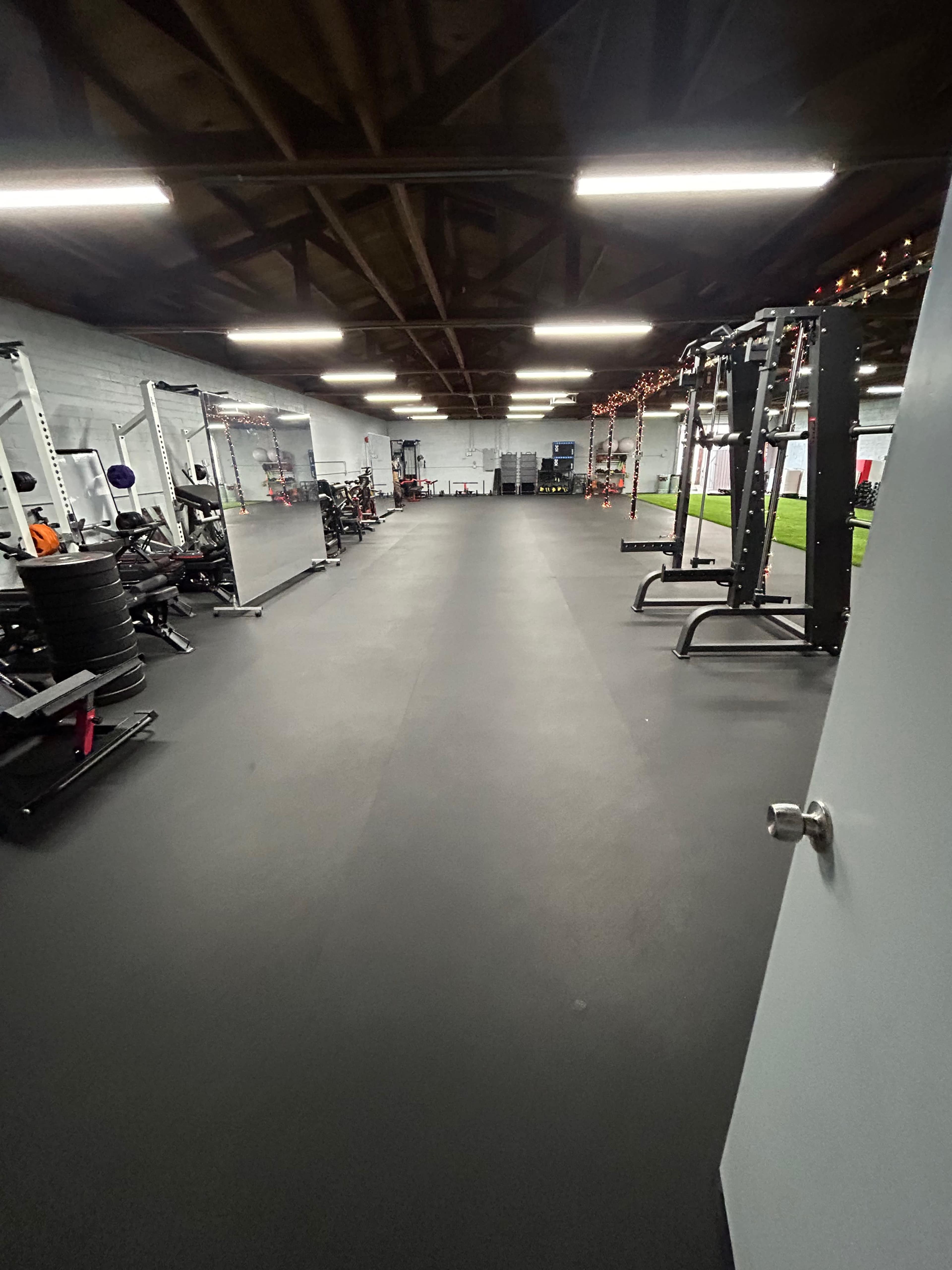 An empty gym interior with various fitness equipment arranged on both sides and a smooth black floor.