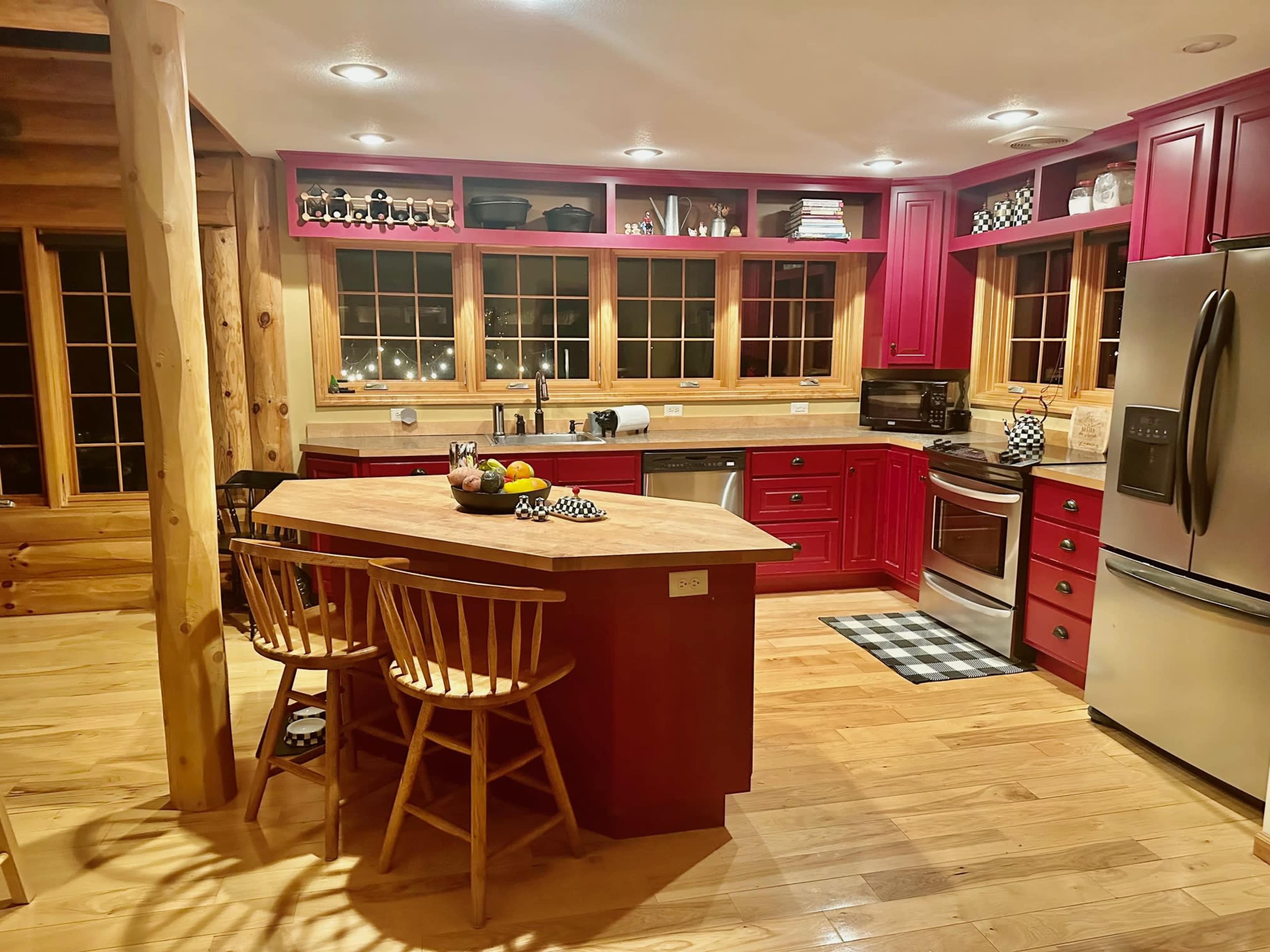 The kitchen features red cabinetry, wooden accents, and a central island with seating, illuminated by overhead lights.