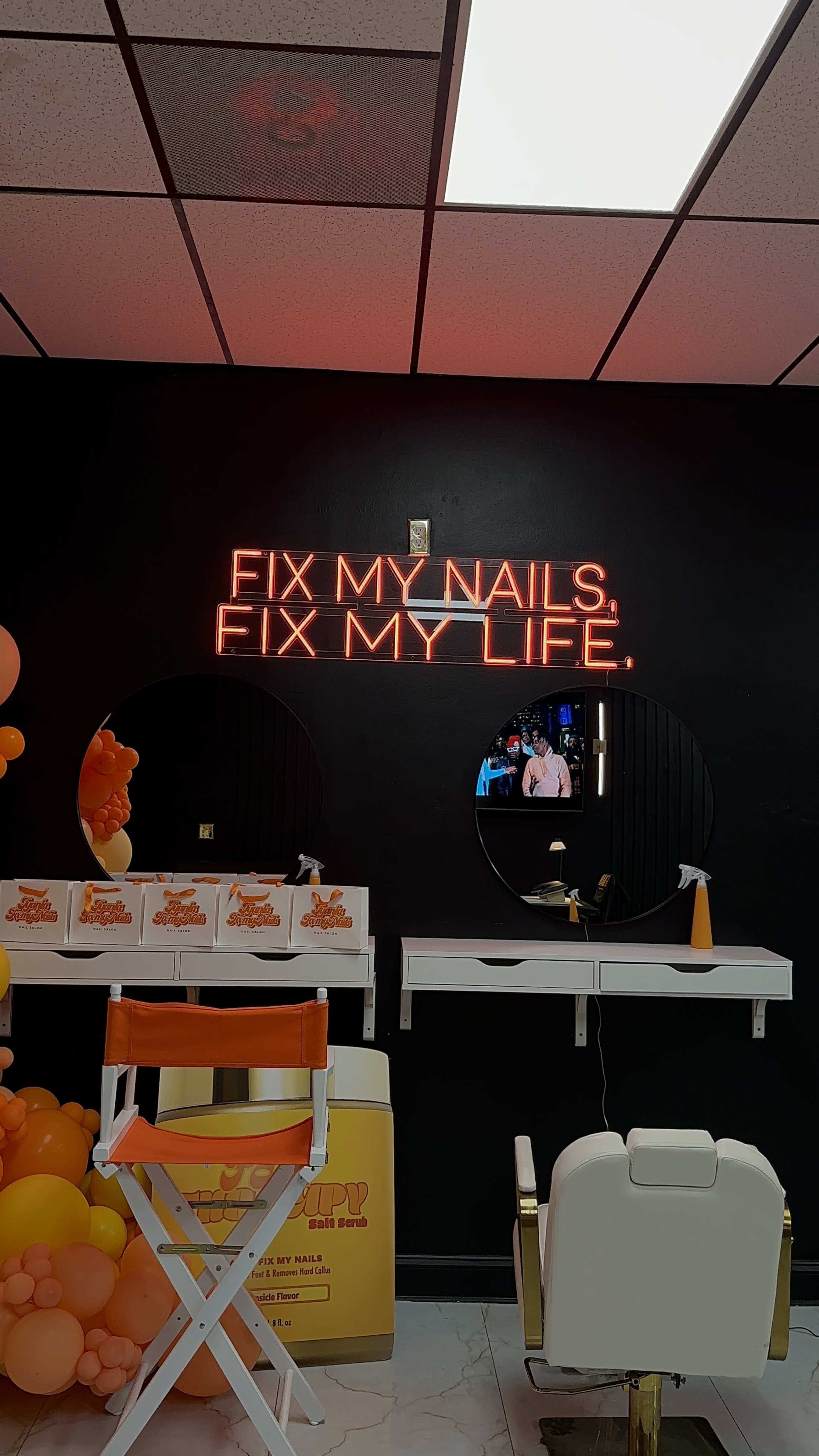 The image shows a nail salon with a black wall featuring a neon sign that reads "FIX MY NAILS, FIX MY LIFE," and two circular mirrors.