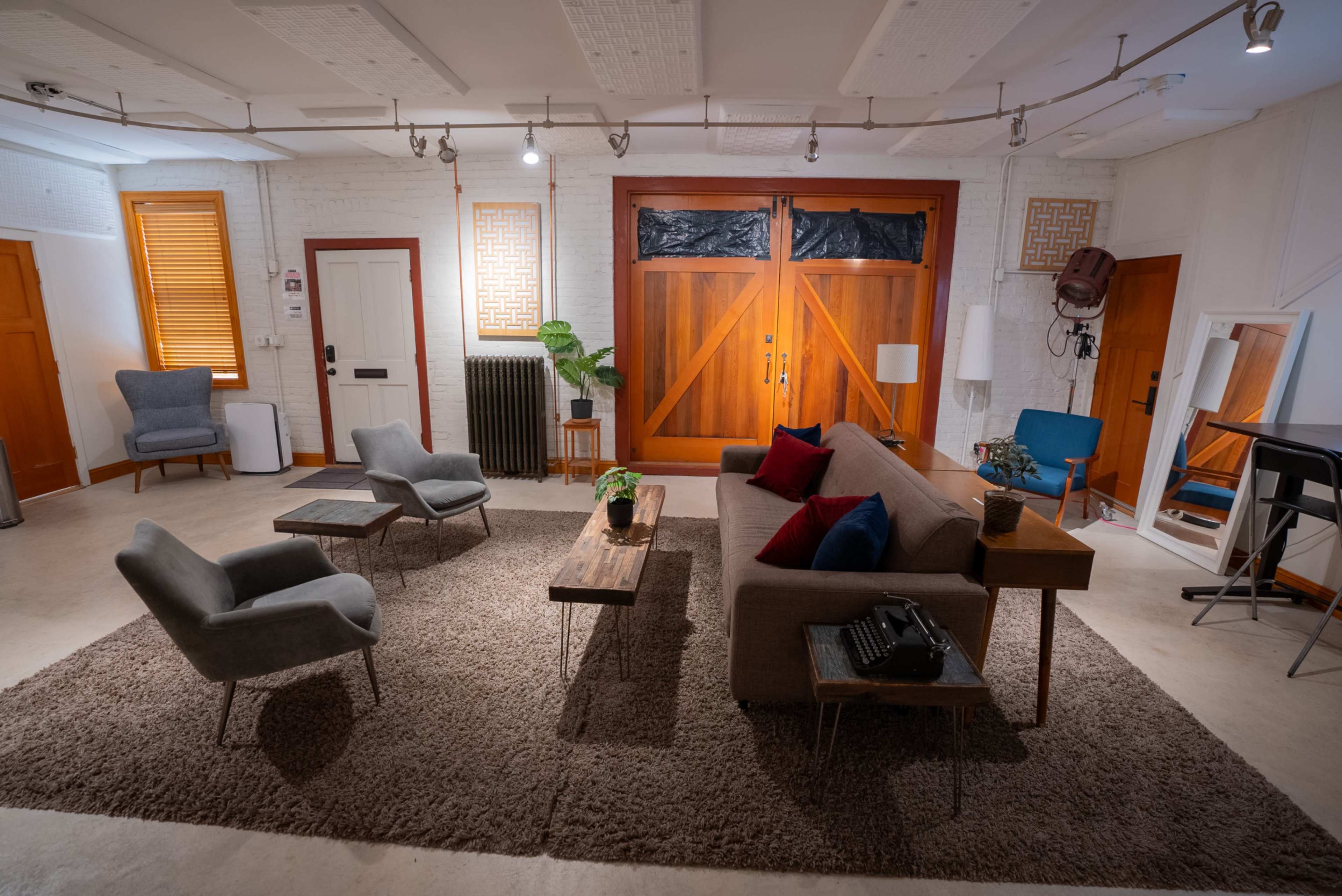 A cozy living room features a sofa and armchairs arranged around a coffee table on a large rug, with wooden doors providing a backdrop.