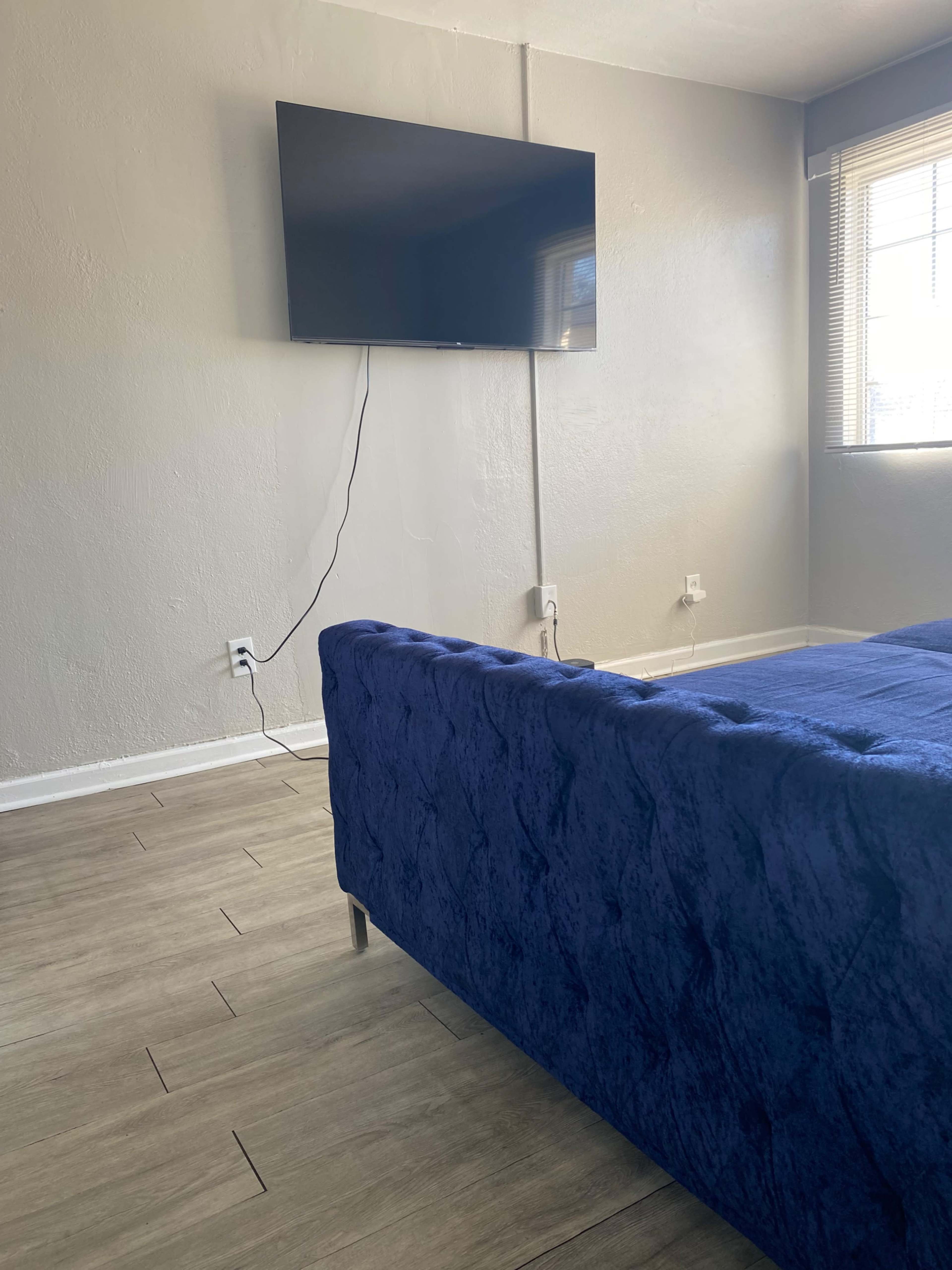 The image shows a living room with a blue tufted sofa and a mounted flat-screen TV on the wall.