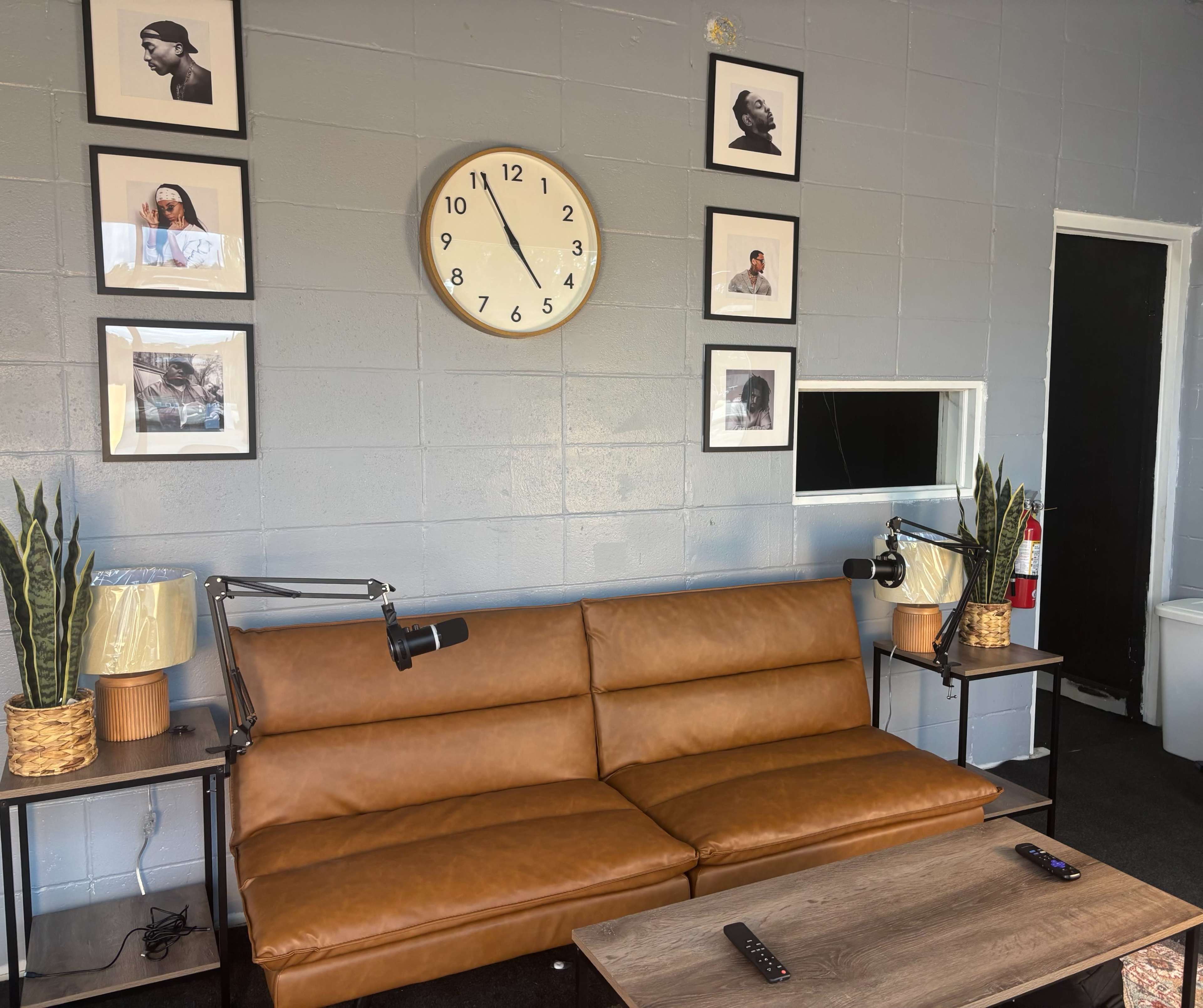 The image shows a modern living room with a brown leather couch, two lamps, a clock on the wall, and framed photographs.
