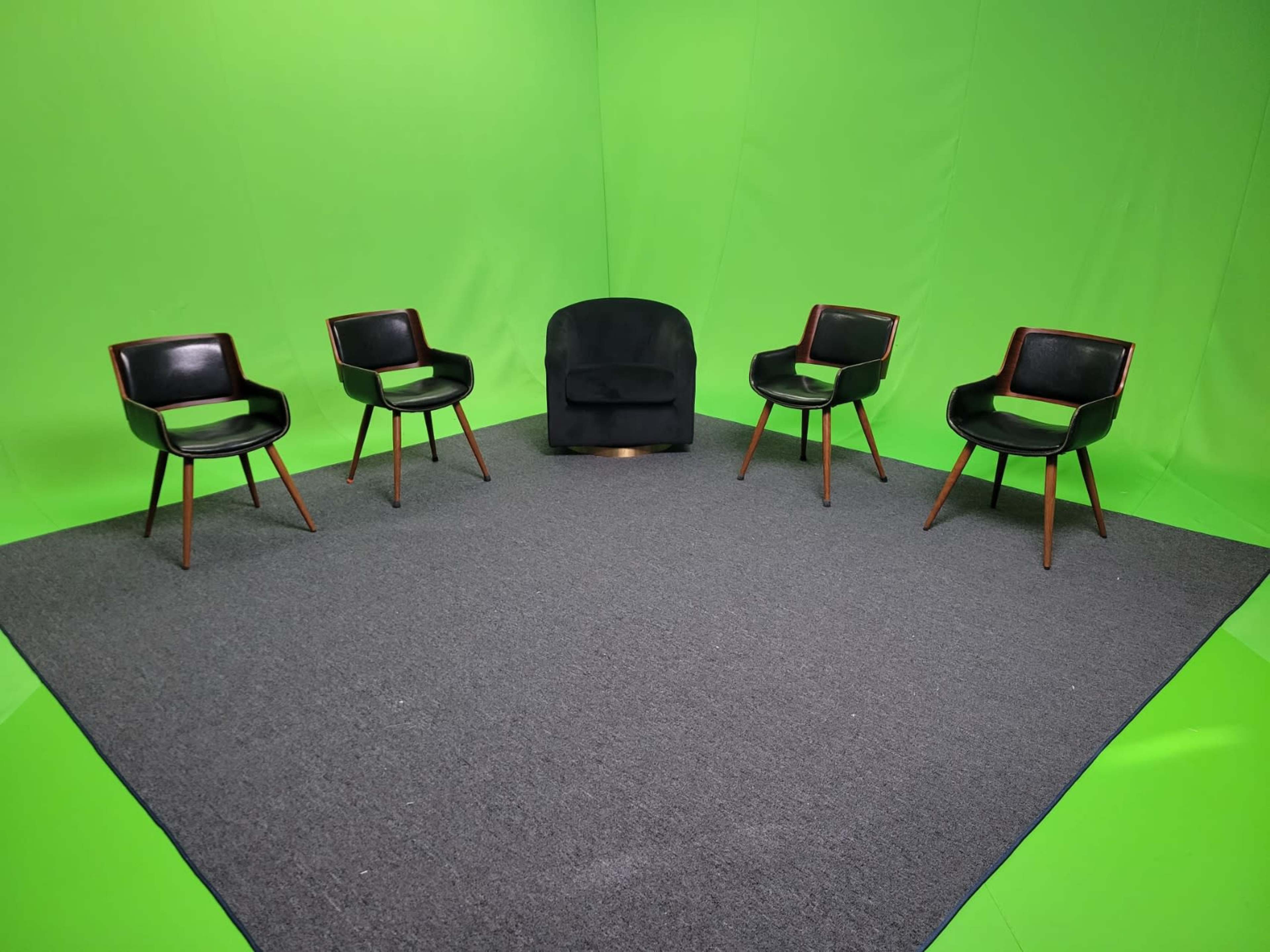A set of five chairs arranged on a gray carpet in front of a green screen backdrop.