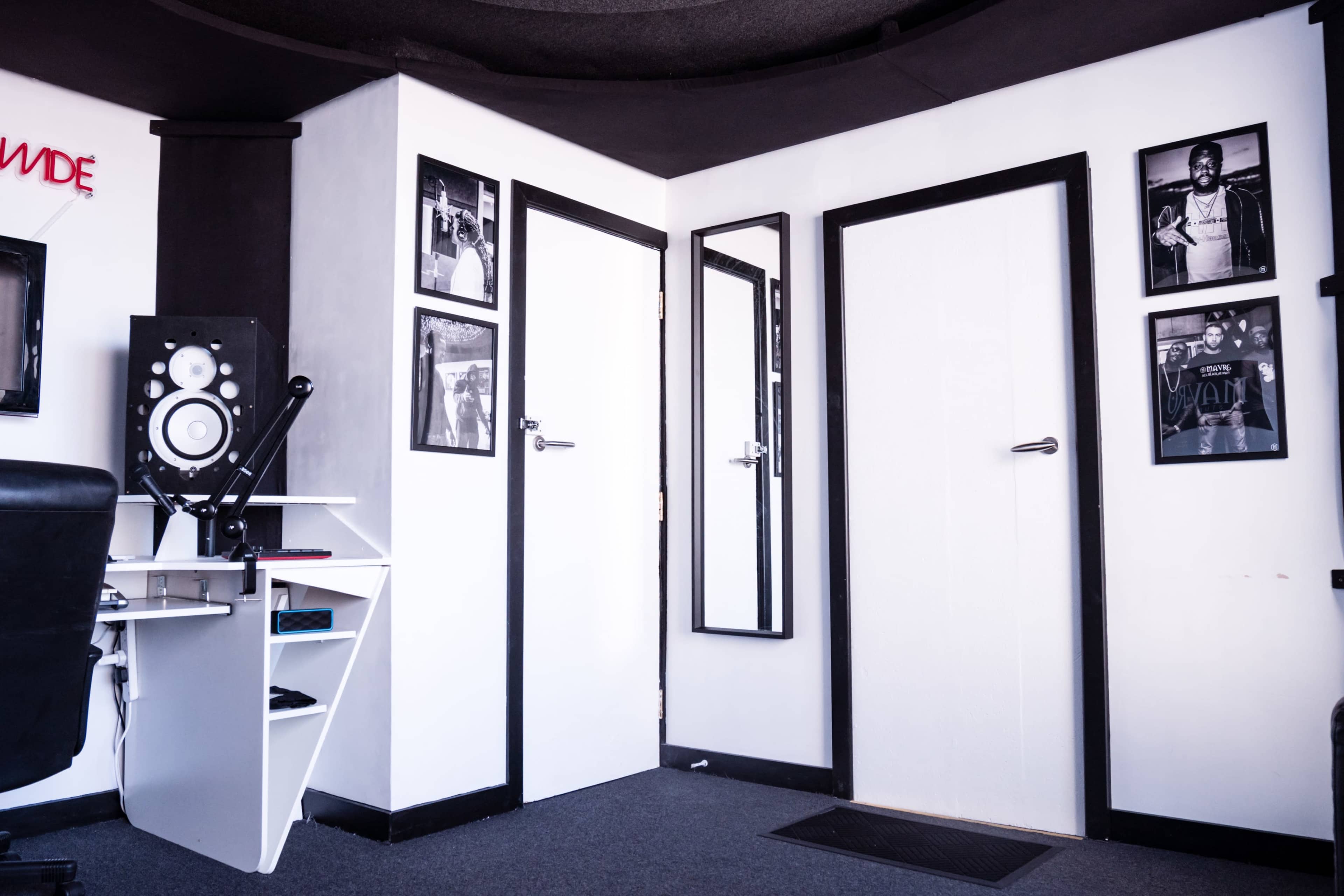 A corner of a room with two doors, a large mirror, a speaker setup, and several framed photographs on the walls.