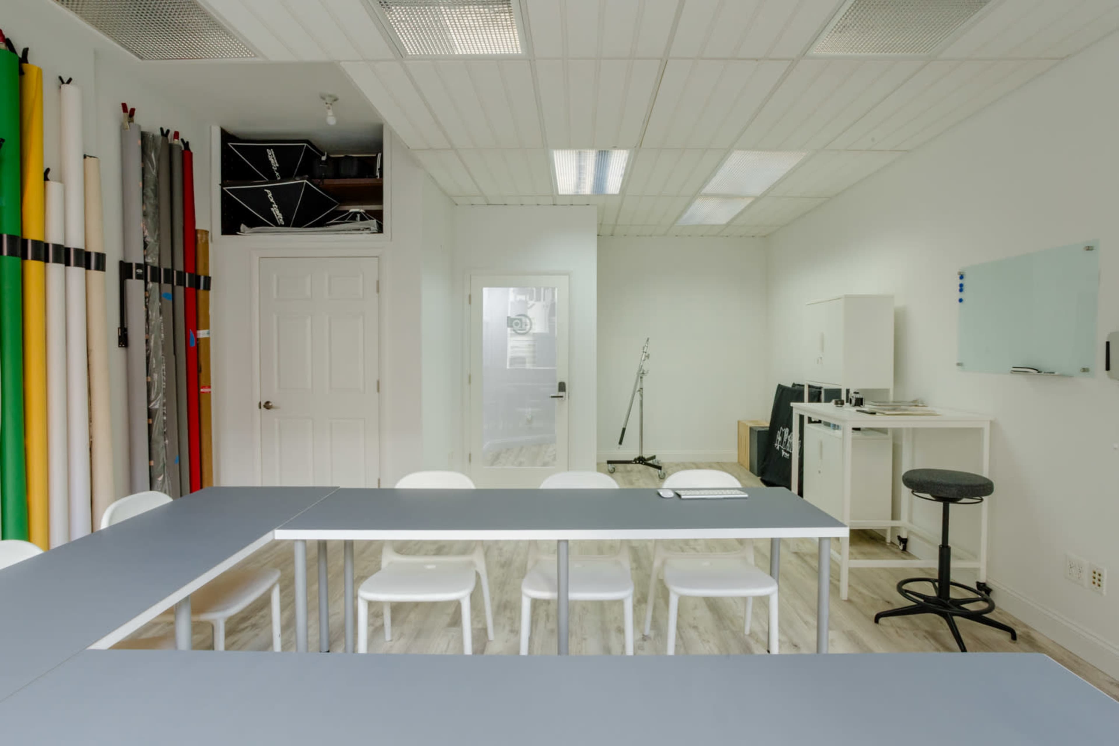A modern, well-lit studio space features a long table surrounded by white chairs, with various photography backdrops stored against one wall.