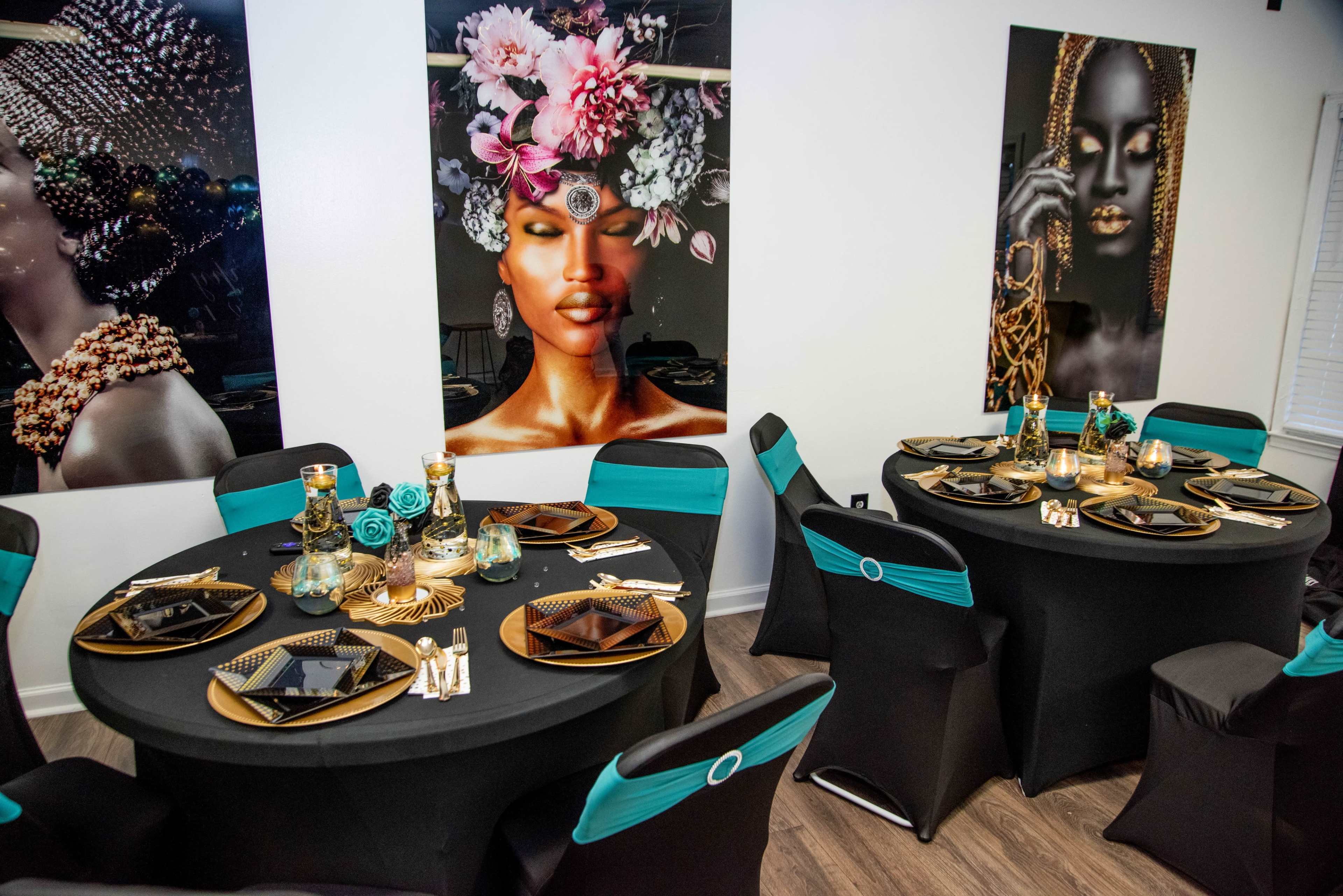 A stylishly decorated dining area featuring two round tables set with black tablecloths, gold and black tableware, and artwork of elegant women on the walls.