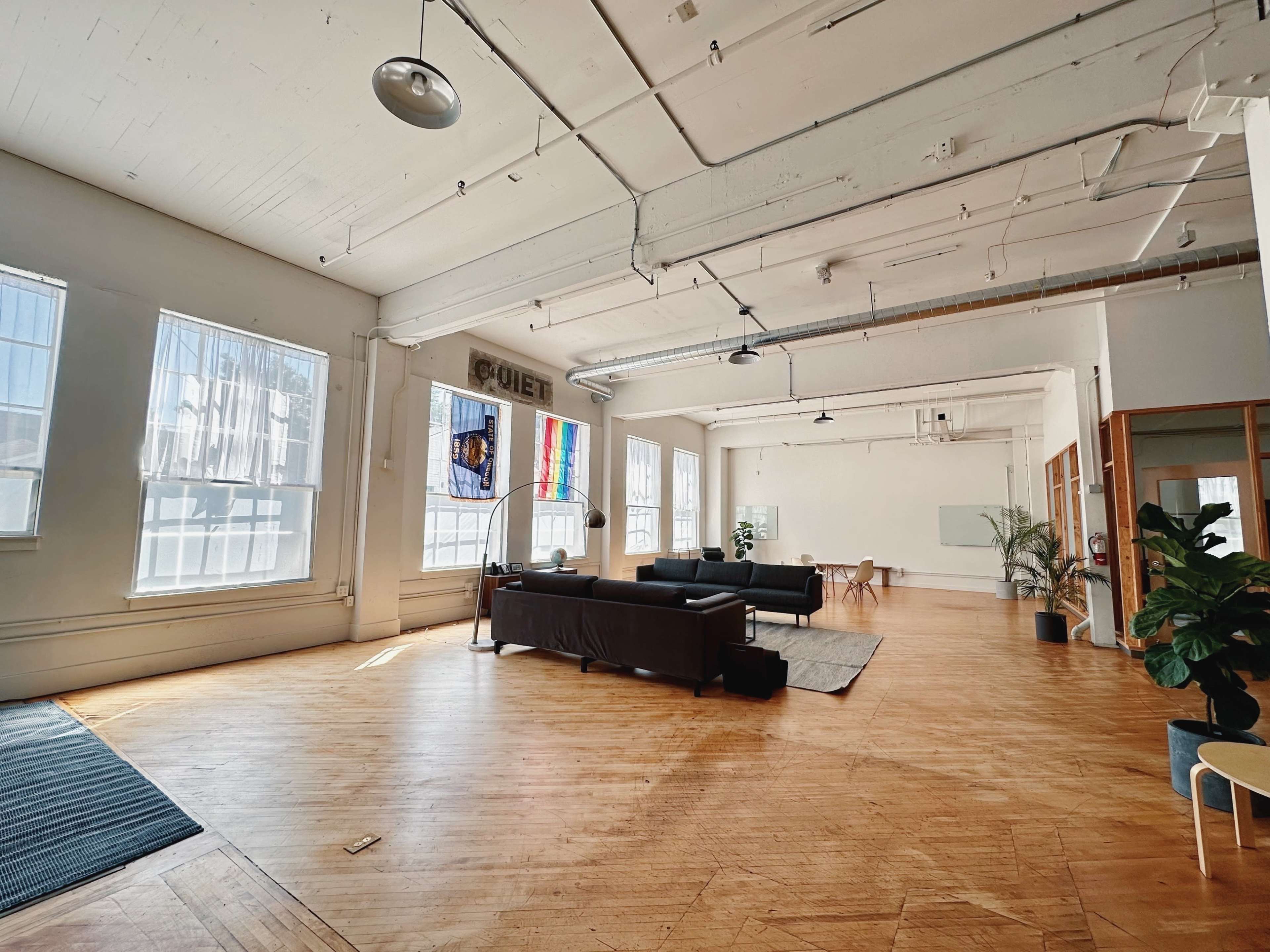 A spacious, well-lit interior with wooden flooring, large windows, modern furniture, and decorative plants.