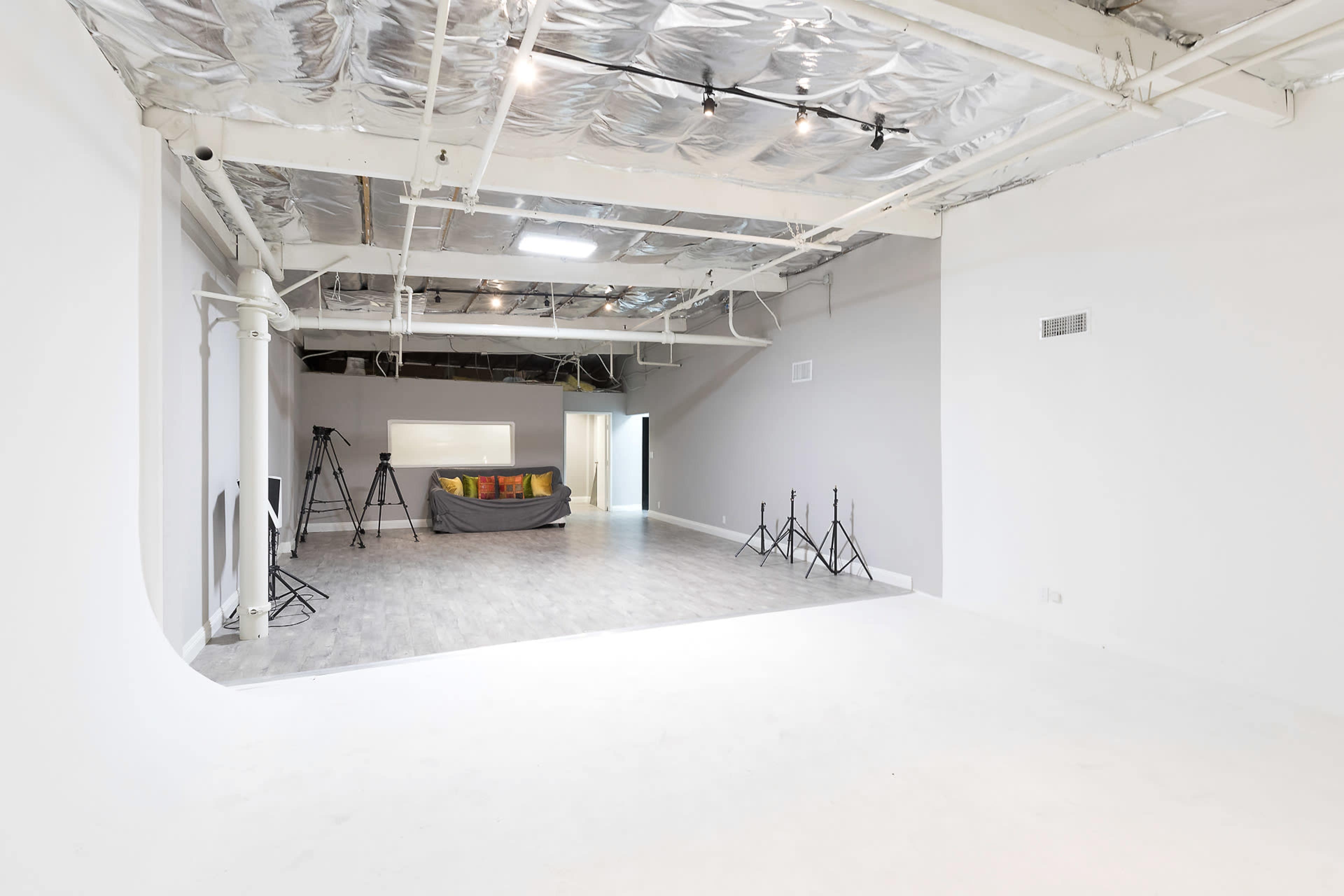 A spacious, unfinished studio with a light-colored floor, exposed ceiling, and several standing tripods in the background.